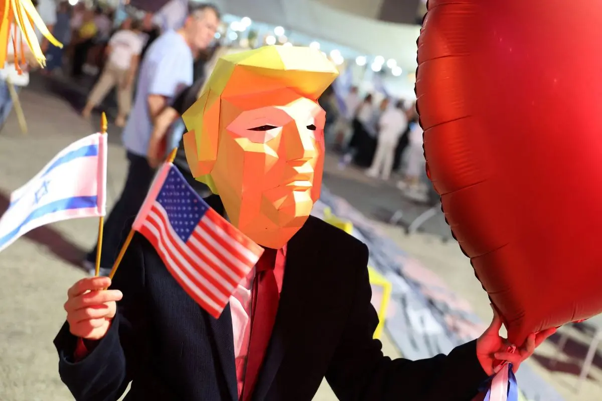 A man wearing a mask in effigy of US President Donald Trump, holds a heart-shaped balloon during a rally organised by families of hostages held in the Gaza Strip (Photo: AFP)