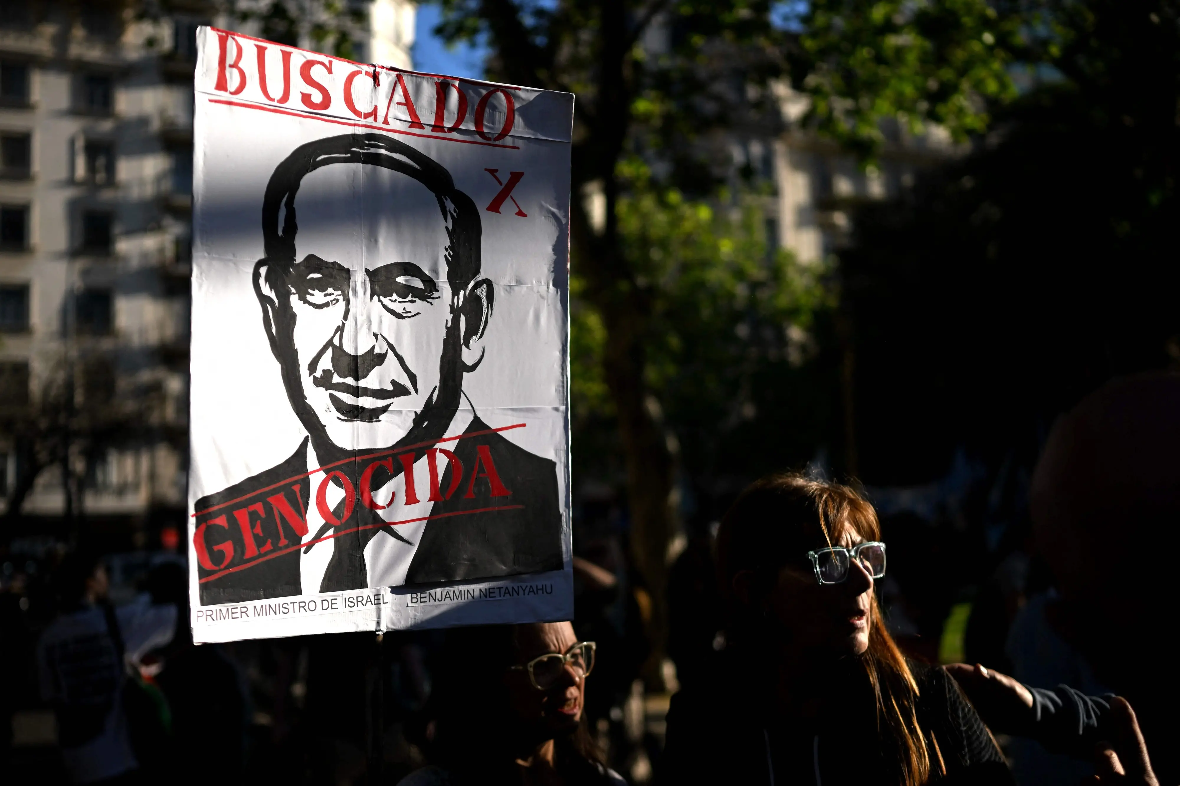 Demonstrators show a sign depicting Israeli Prime Minister Benjamin Netanyahu with the words "Wanted" and "Genocidal" during a march in Buenos Aires. | Photo: AFP