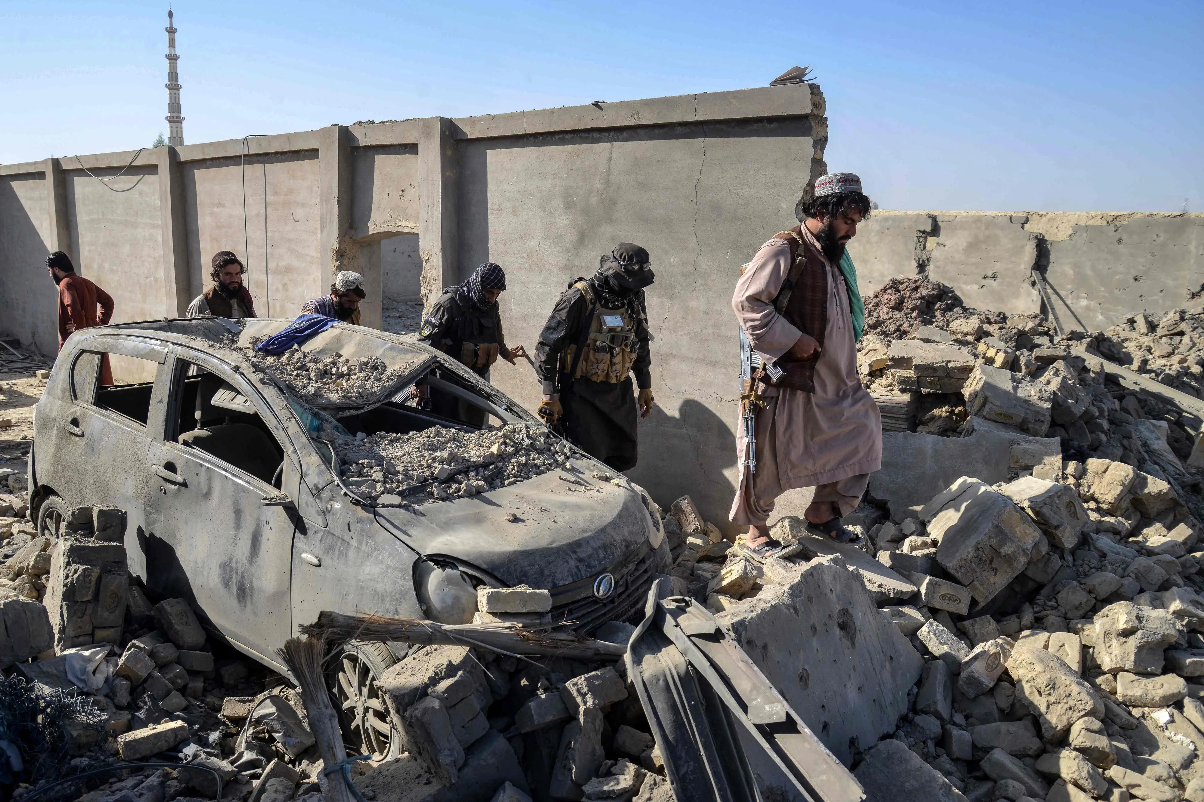 Taliban security personnel walk past a damaged car in the Spin Boldak district of Kandahar province on October 16, 2025, a day after the cross-border clashes between Afghanistan and Pakistan. | Photo: AFP