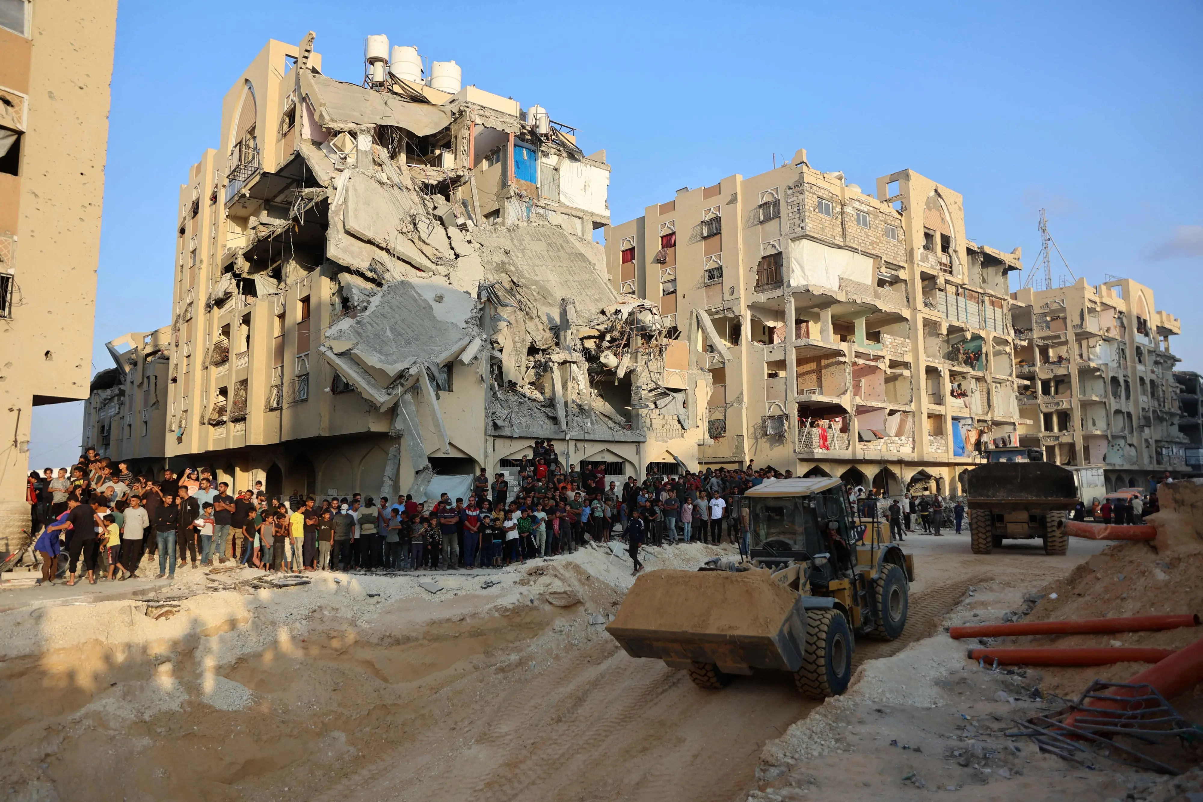 People watch as Palestinians use an excavator to dig deep into the ground, reportedly searching for bodies in Khan Yunis in the southern Gaza Strip,on October 17, 2025. | Photo: AFP