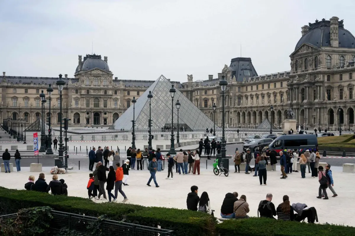 Tourists and visitors walk in front of the Louvre Museum next to French police officers (C) after the museum was closed following a robbery (Photo: AFP)