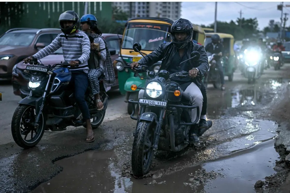 Commuters drive over potholes on a road in Bengaluru on September 23, 2025. (Photo by Idrees MOHAMMED / AFP)