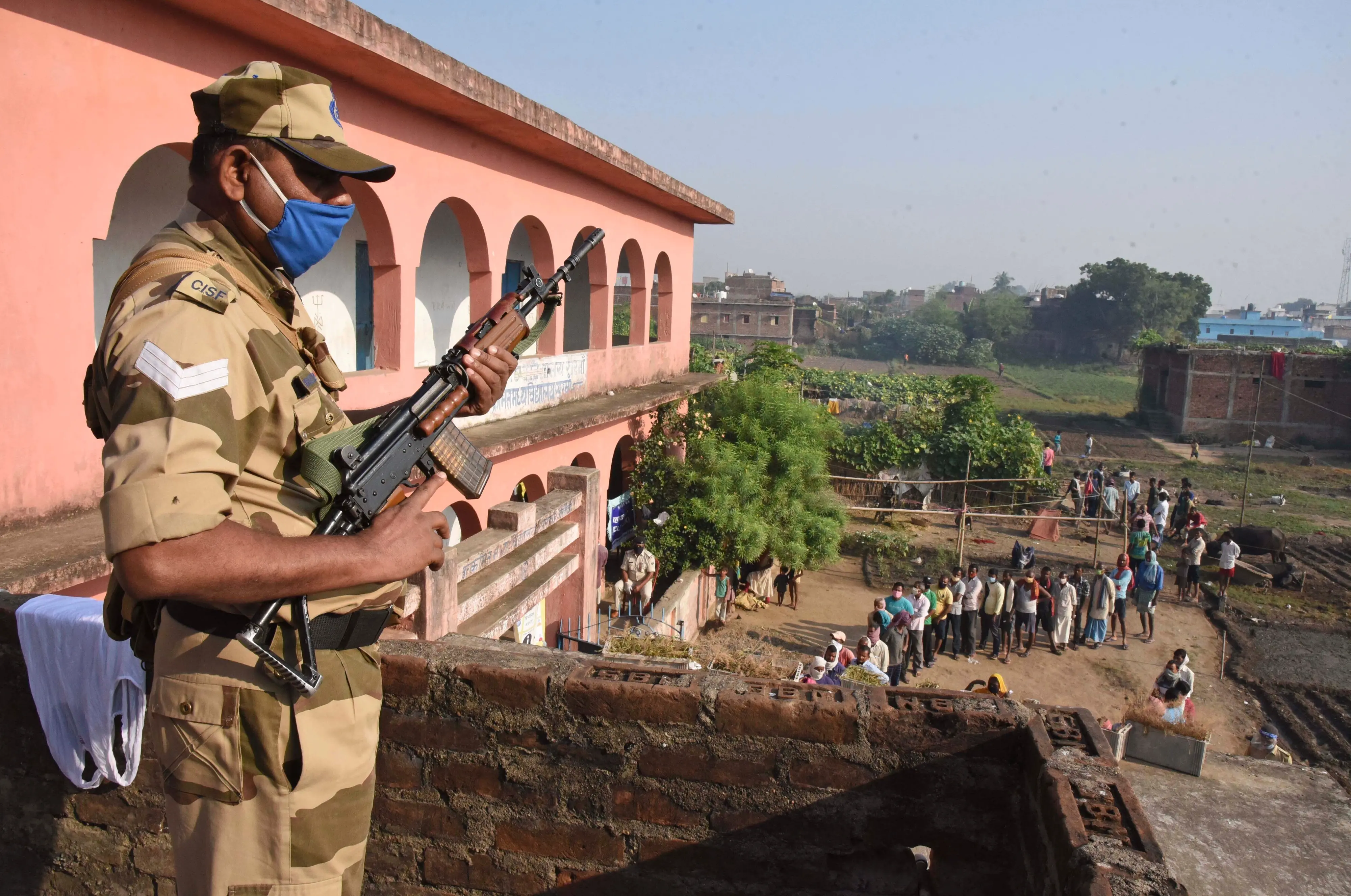 A security officer stands guard as voters stand in a queue outside a polling station in Bihar | Photo: AP