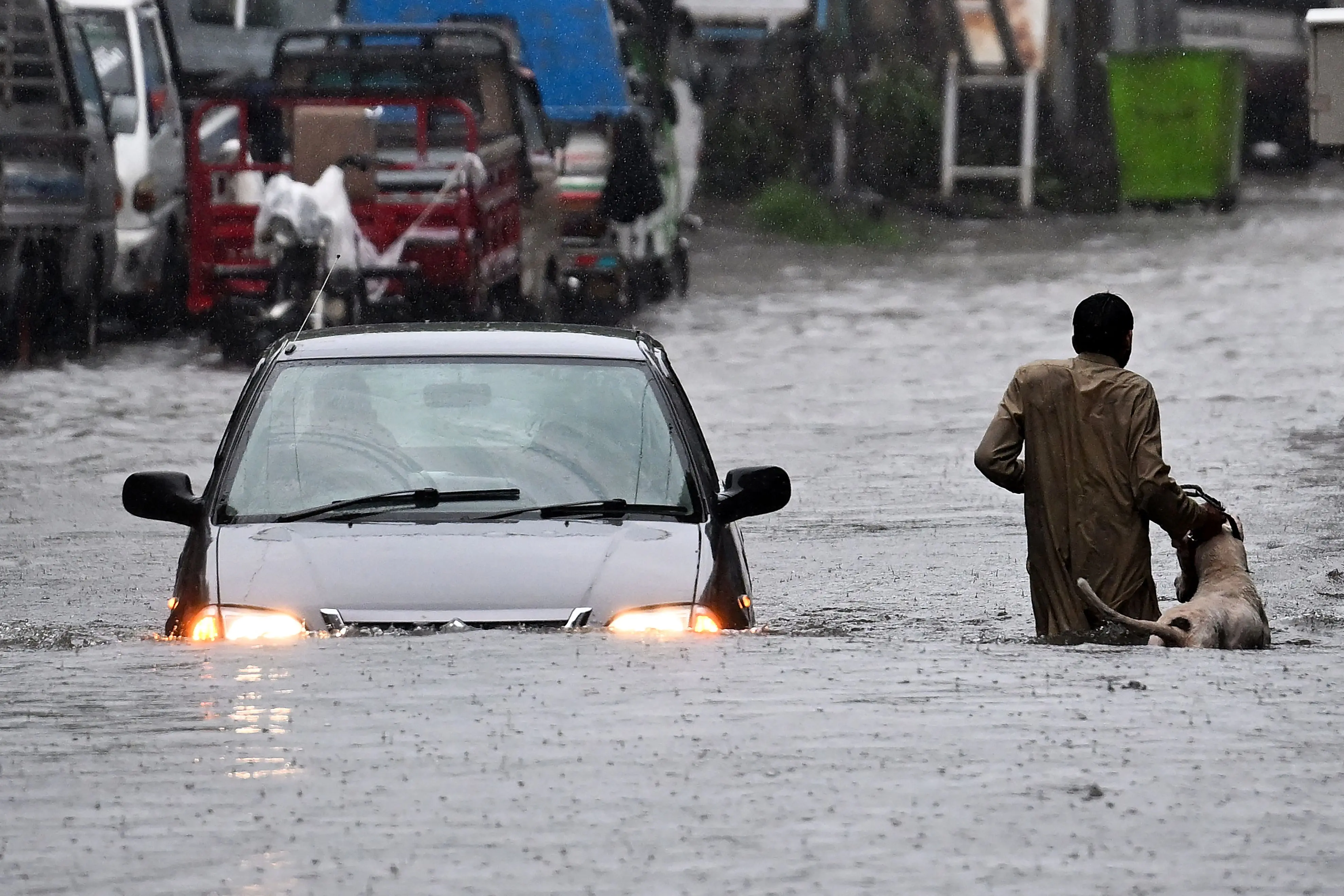 A man along with his dog while a car wade through a flooded street during heavy monsoon rains in Rawalpindi on July 17 | Photo: AFP