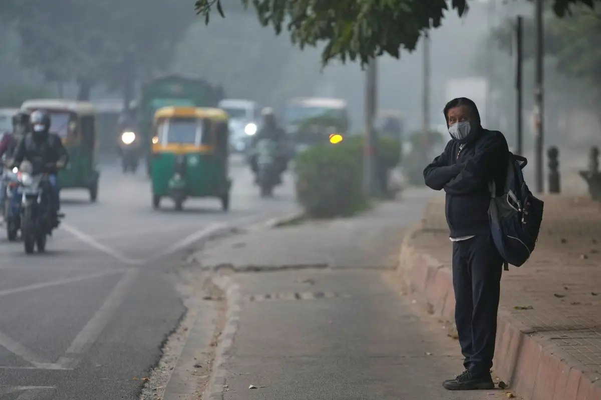 A commuter waits for transport wearing a face mask on a fog-filled morning in New Delhi