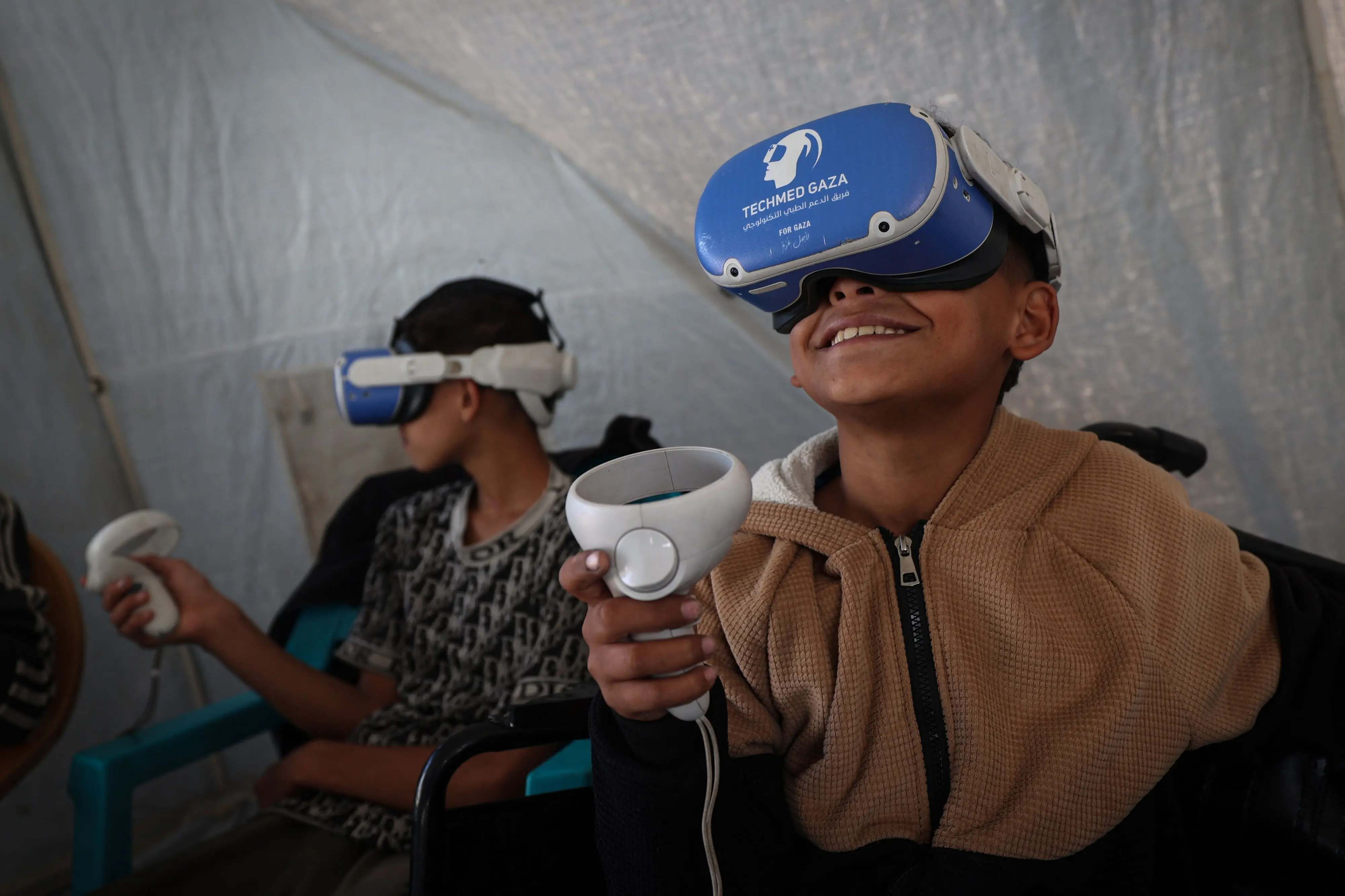 Palestinian children wearing goggles and holding a joy stick experience virtual reality in the city of Al-Zawayda, in the central Gaza Strip | Photo: AFP