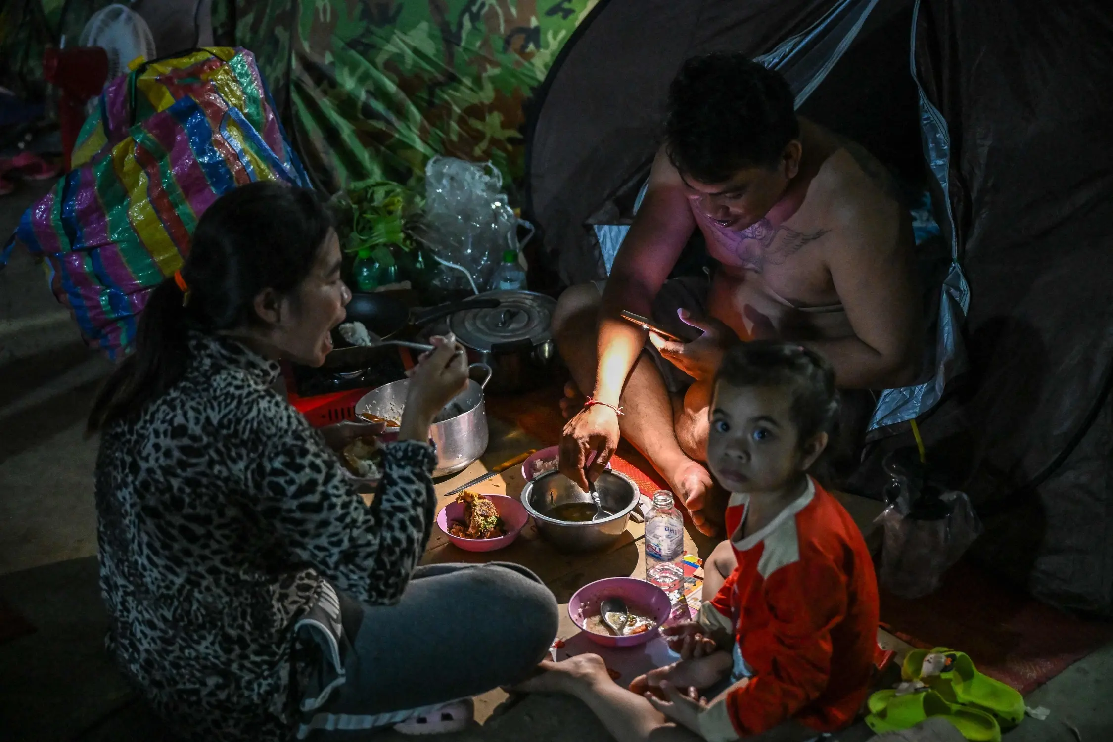 A displaced family uses a flashlight as they eat a meal at a temporary camp in Banteay Meanchey province, Cambodia | Photo: AFP