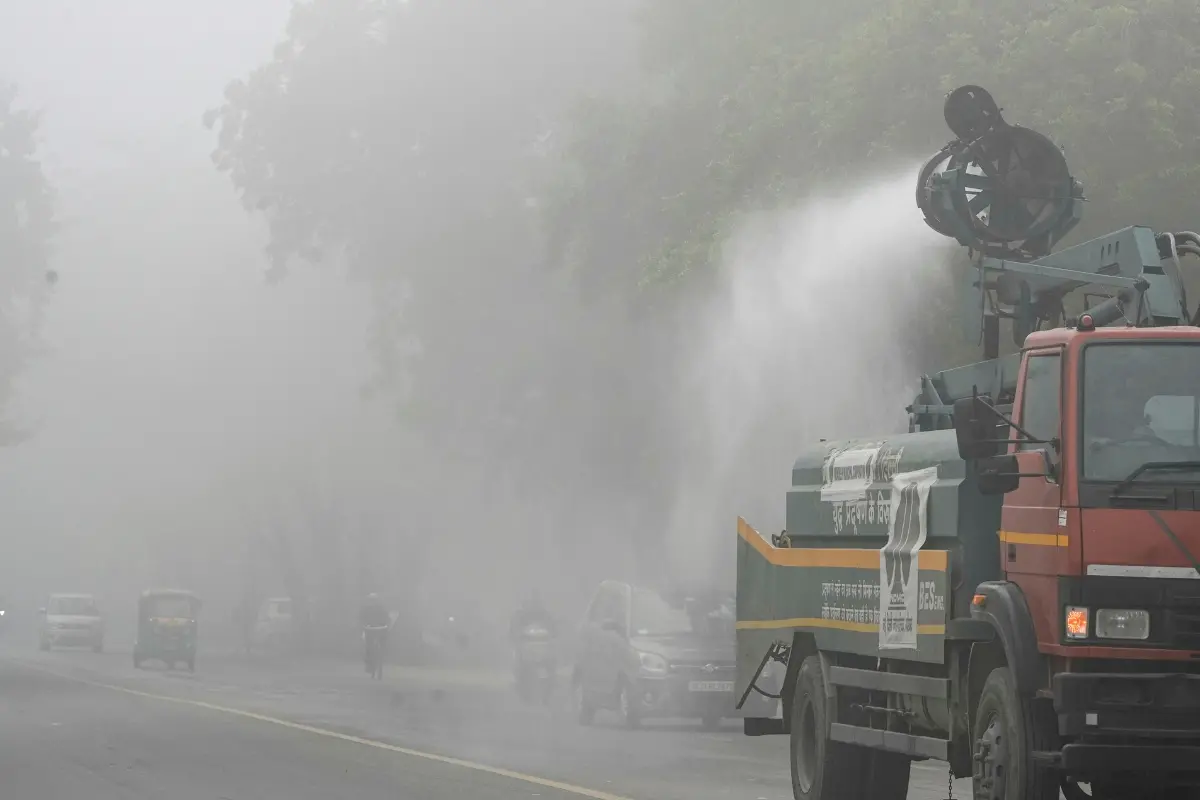 A municipal truck sprays water on a roadside to suppress dust and pollution amid dense foggy conditions, in New Delhi, Monday | Photo: PTI