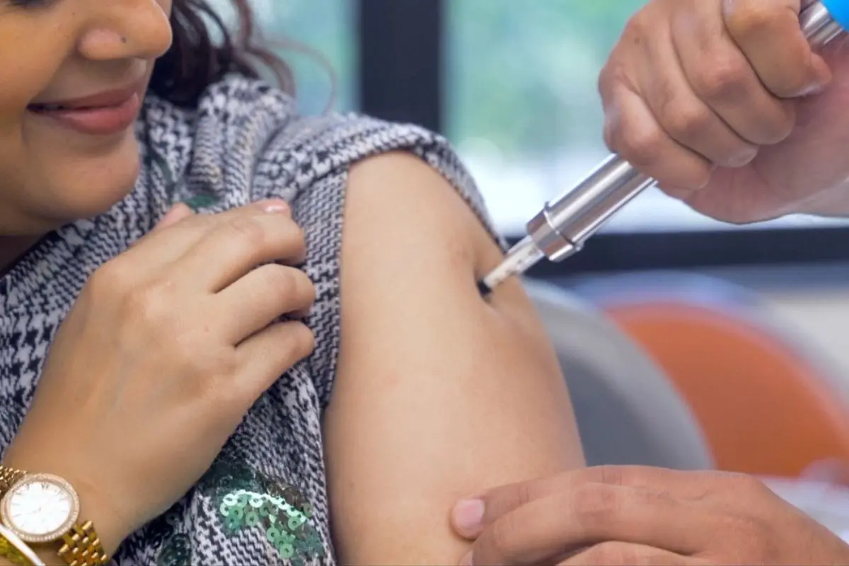 A healthcare professional administers a needle-free injection to a woman using a high-pressure jet system, delivering the dose without a traditional needle in a clinical setting. Representative photo: MoesArt