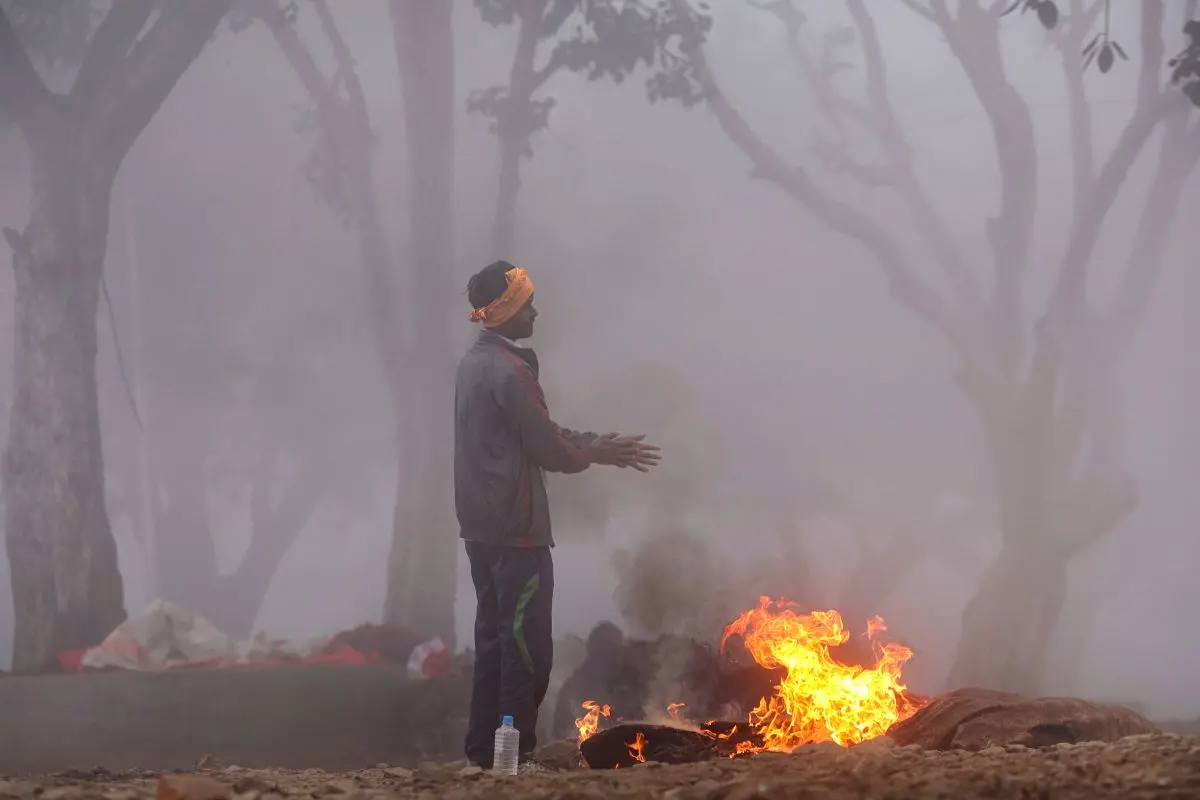 A man warms himself near a small fire on a cold and foggy winter morning in Prayagraj, Thursday, December 25, 2025. (PTI Photo)