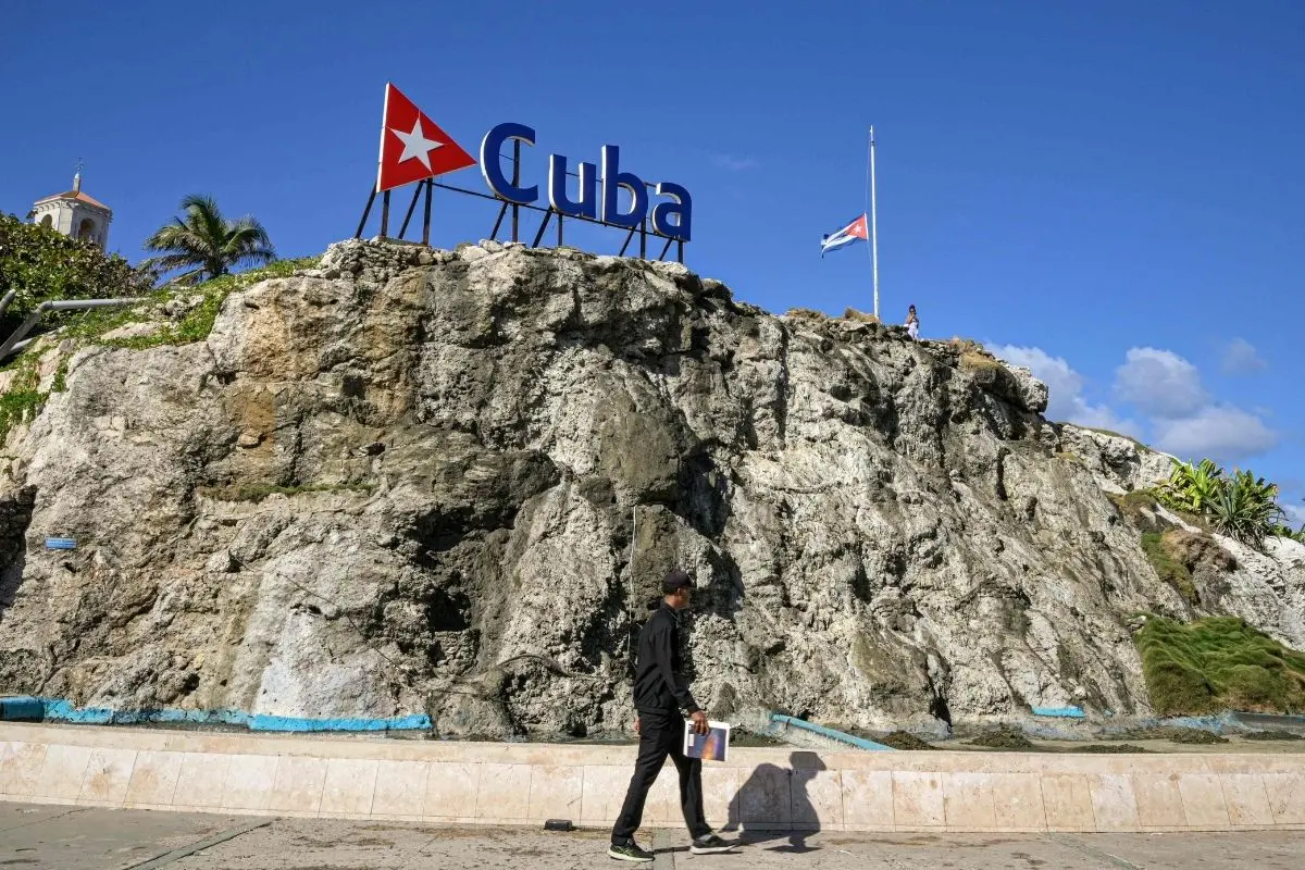 A Cuban man walks by a Cuba sign and national flag at half-mast in Havana on January 5, 2026. Havana declared two days of national mourning as of January 5 after a total of 32 Cubans were killed during the US attack on Caracas that culminated in the capture of Venezuela's president Nicolas Maduro. | Photo: AFP
