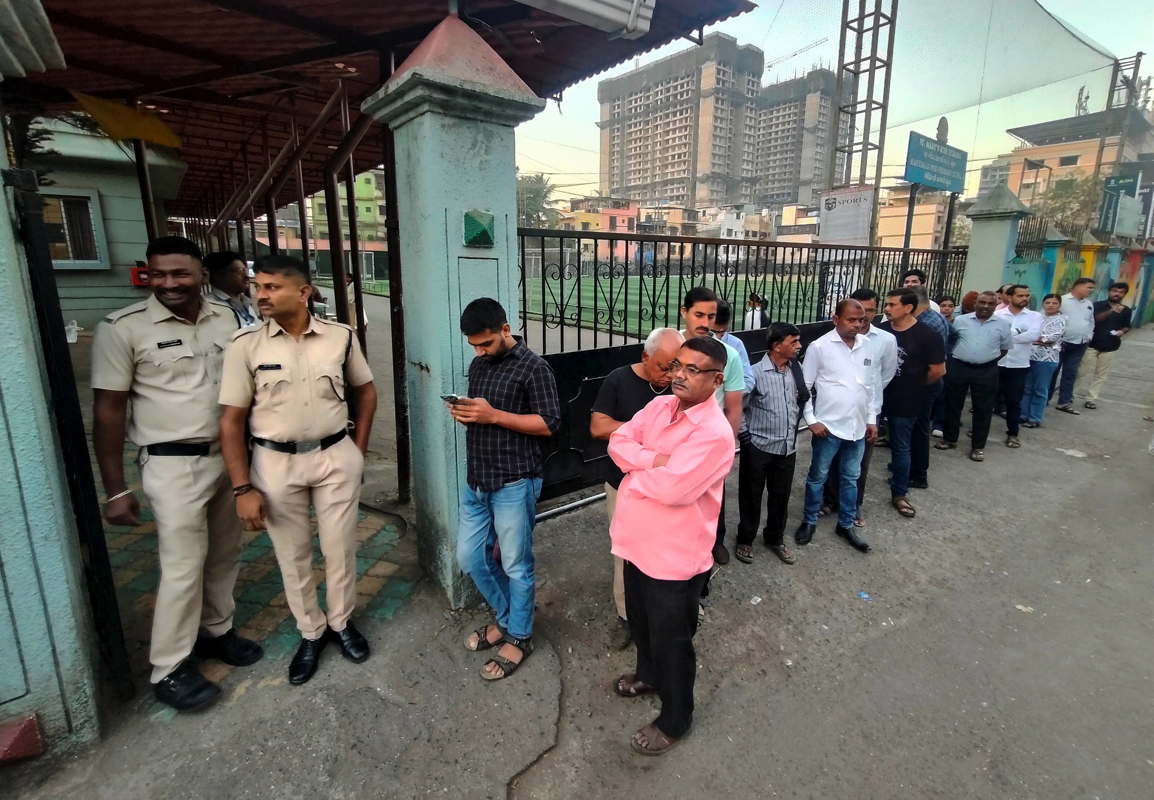 Police personnel stand guard as people wait in a queue to cast votes during the Navi Mumbai Municipal Corporation (NMMC) elections, at a polling station at Kopar Khairane, in Navi Mumbai | PTI