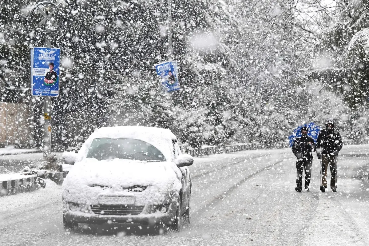 A car covered in snow rides along a road during winter's first snowfall in Srinagar