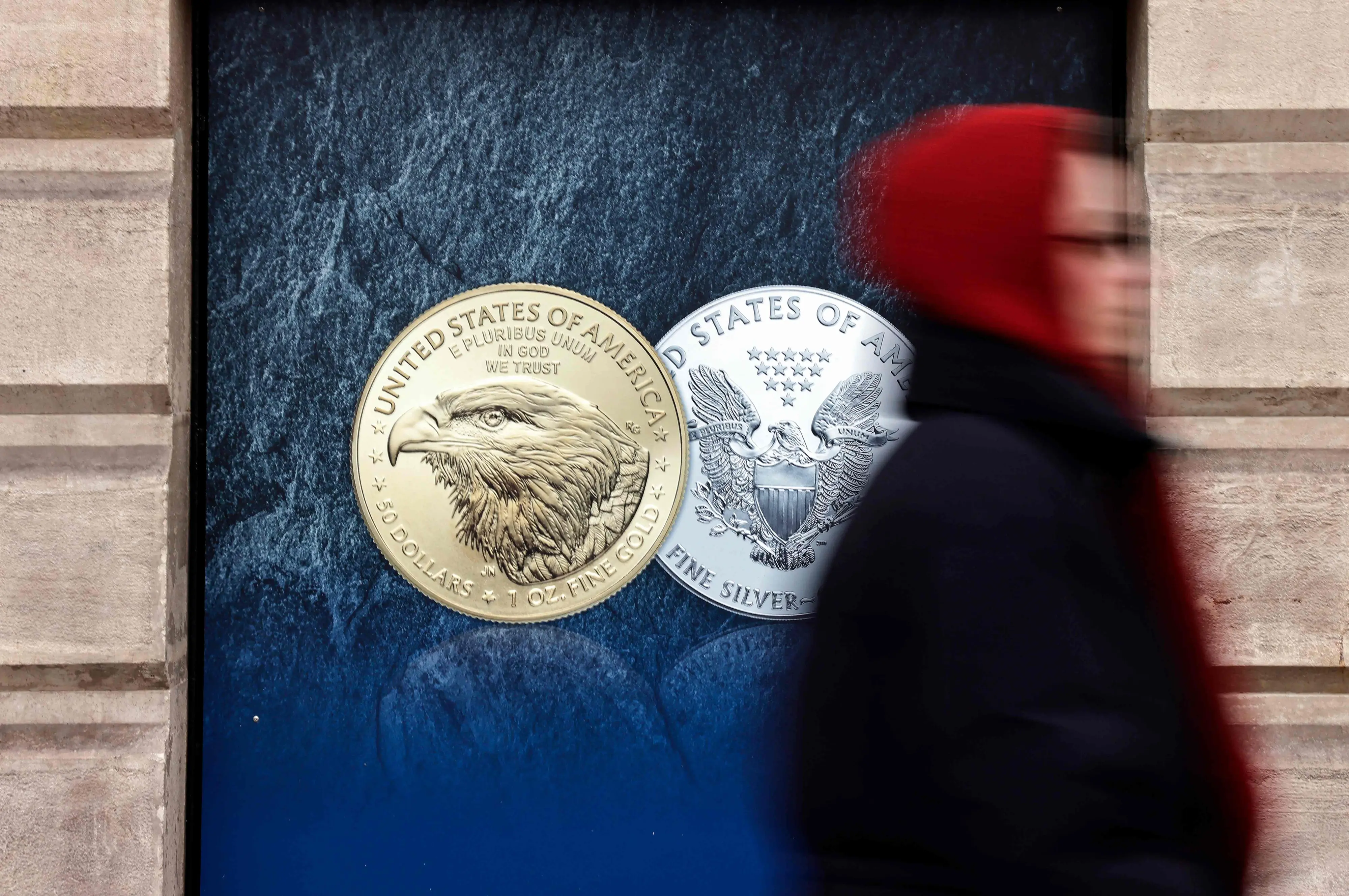 A person walks past a poster showing 'American Eagle' gold and silver bullion coins at a gold dealer's window in Madrid, on January 30, 2026 | AFP