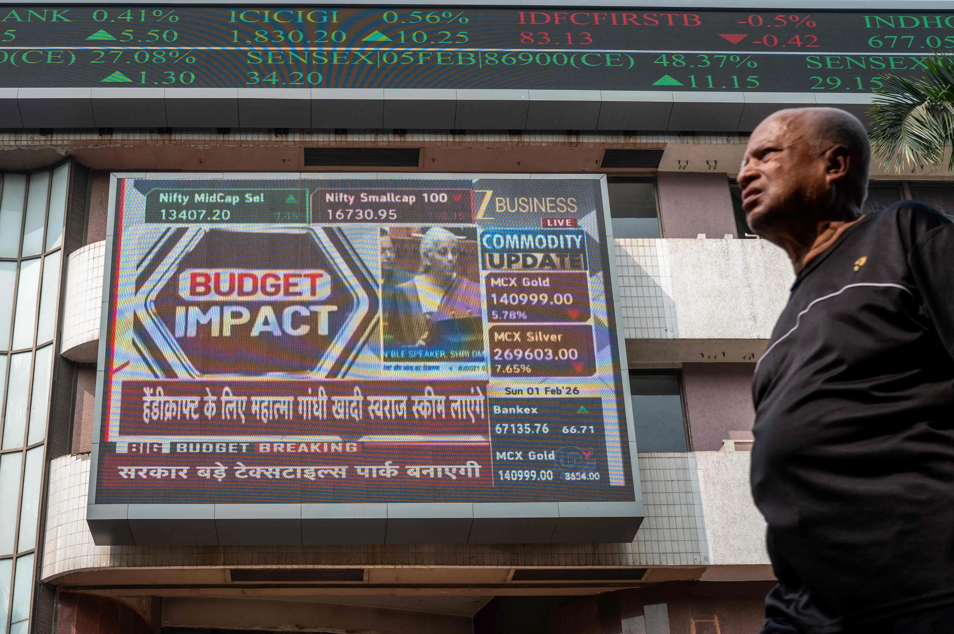 A pedestrian walks past a digital screen displaying a broadcast of the budget speech by Indian Finance Minister Nirmala Sitharaman | AFP