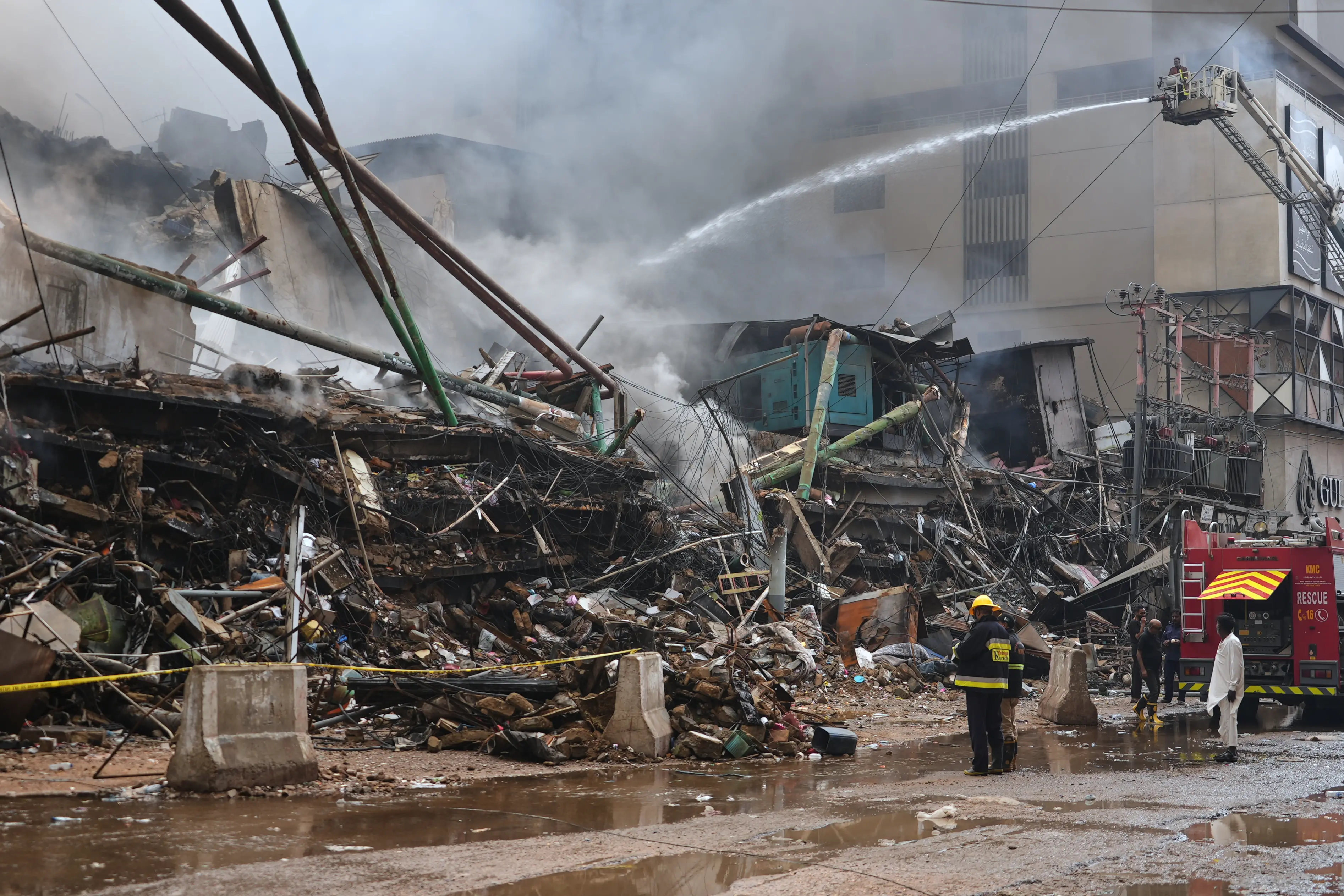 Firefighters examine the collapsed portion of a multi-story shopping mall following a massive fire that broke out overnight in Karachi | Photo: AP