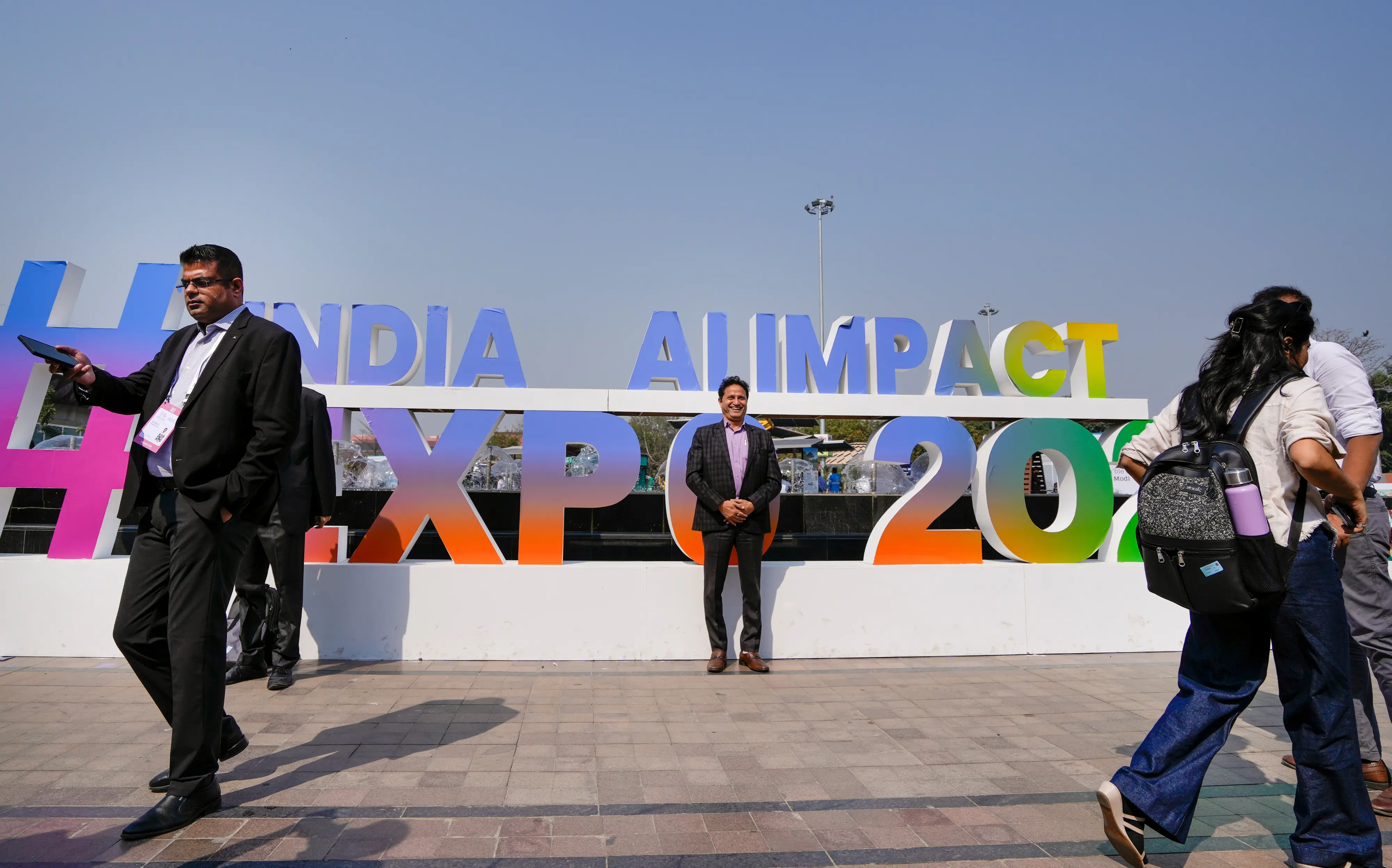 Visitors pose for photographs near the India AI Impact Summit 2026 signage at Bharat Mandapam, in New Delhi | Photo: PTI