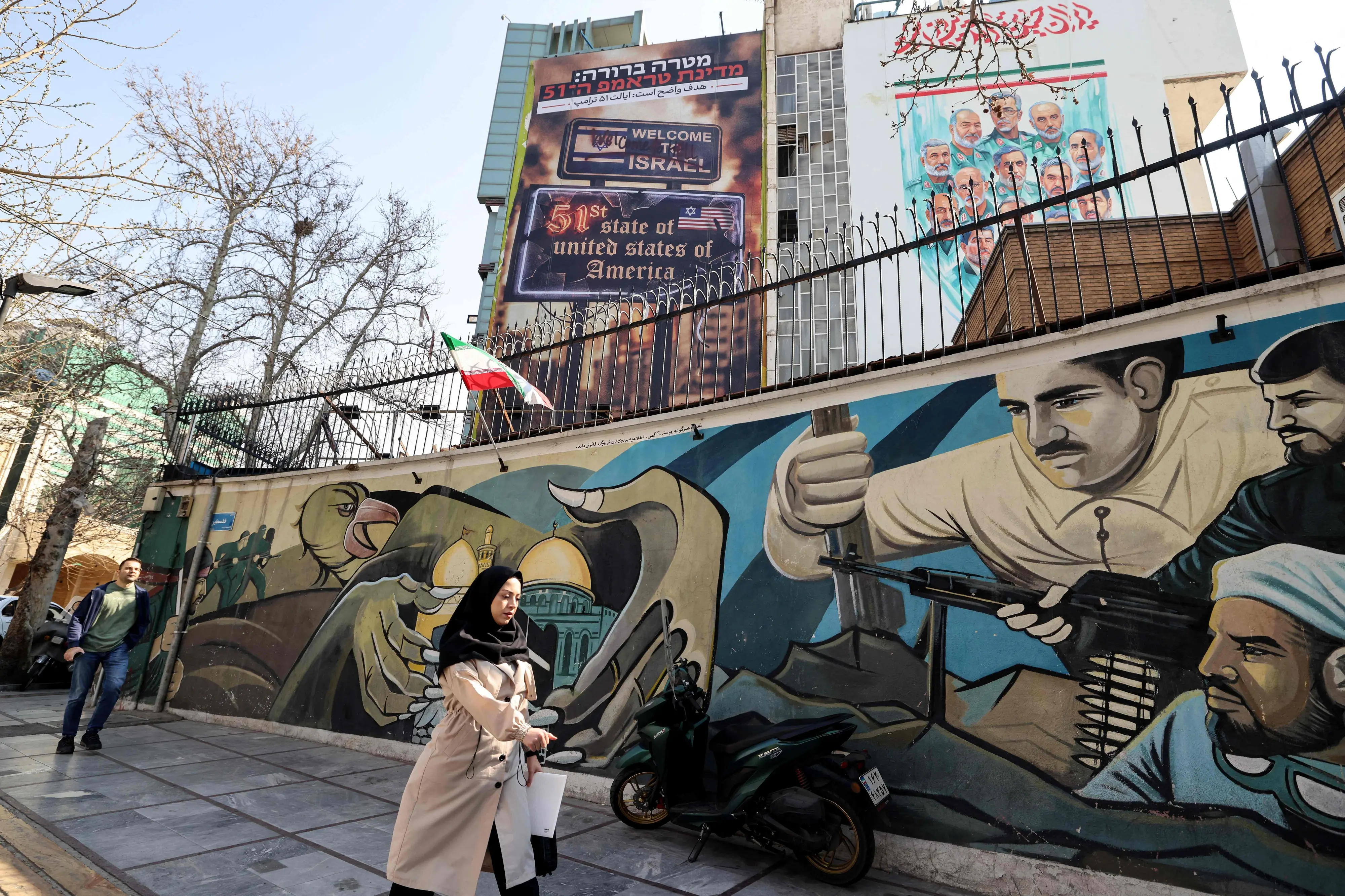 A woman walks past an anti-Israeli and anti-US billboard hanging from a building that reads in Persian "The target is clear: Trump's 51st state" on Palestine Square in Tehran | AFP