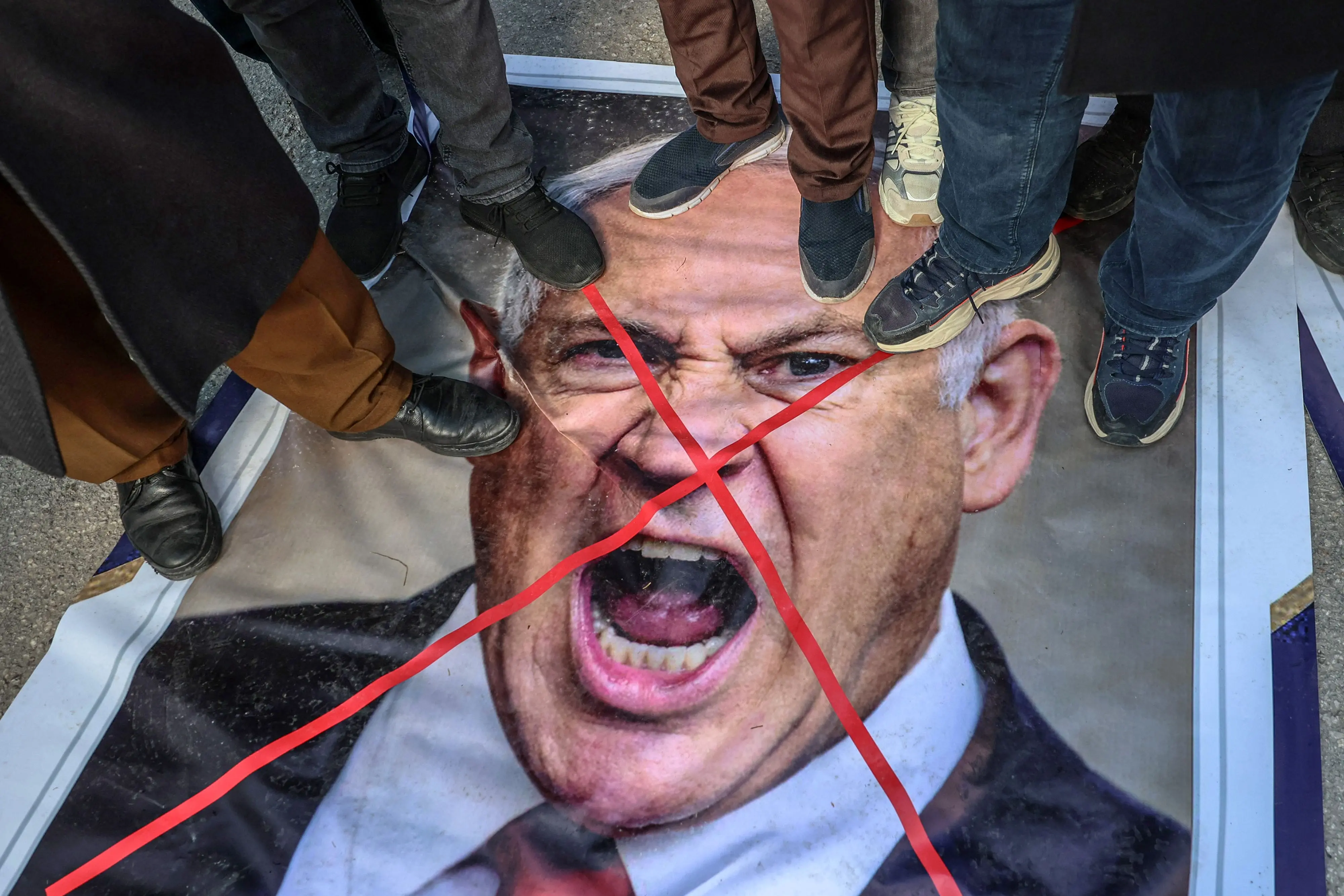 Protestors stand on an image depicting Israeli Prime Minister Benjamin Netanyahu | AFP