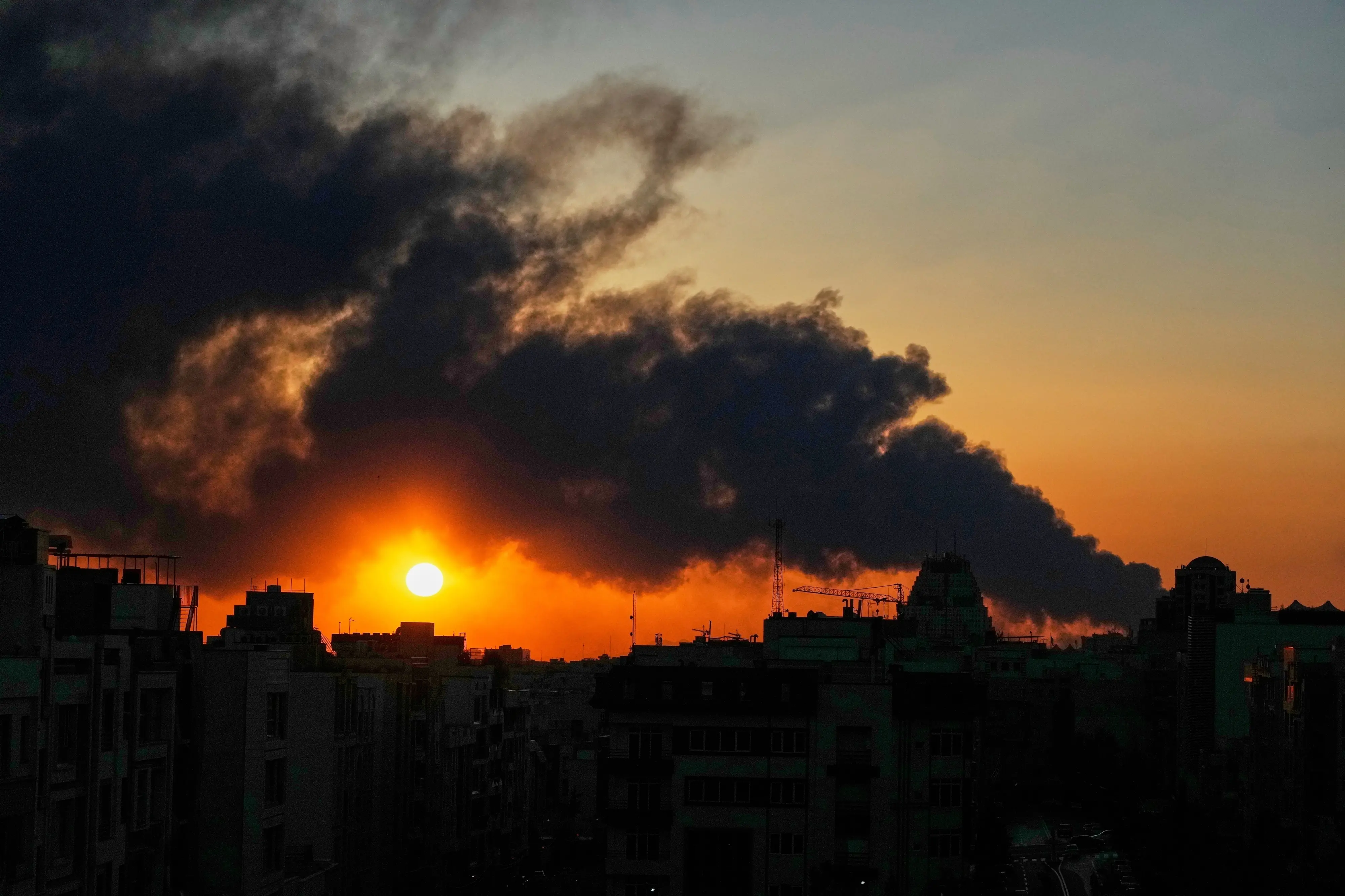 The sun sets behind a plume of smoke rising from a U.S.–Israeli military strike in Tehran, Iran (AP Photo/Vahid Salemi)