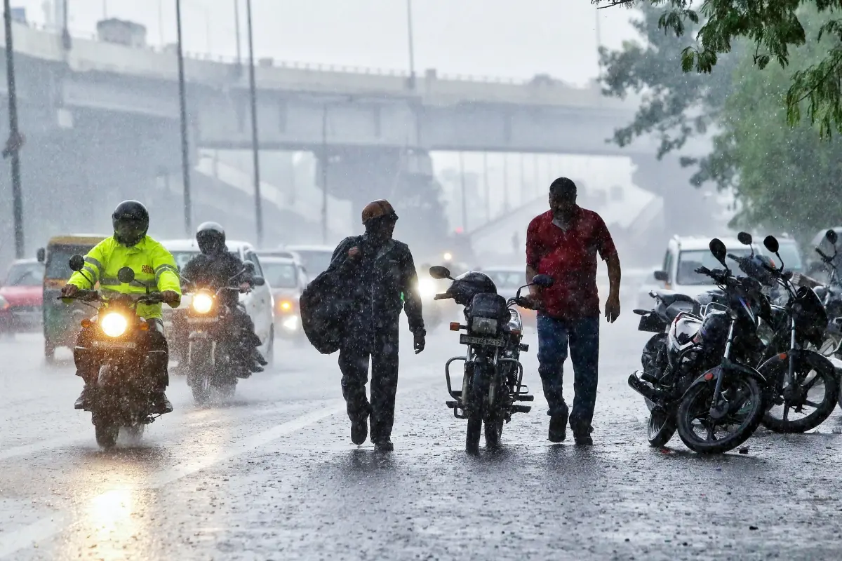Commuters wade their way amid heavy rain, in New Delhi.| Photo: ANI