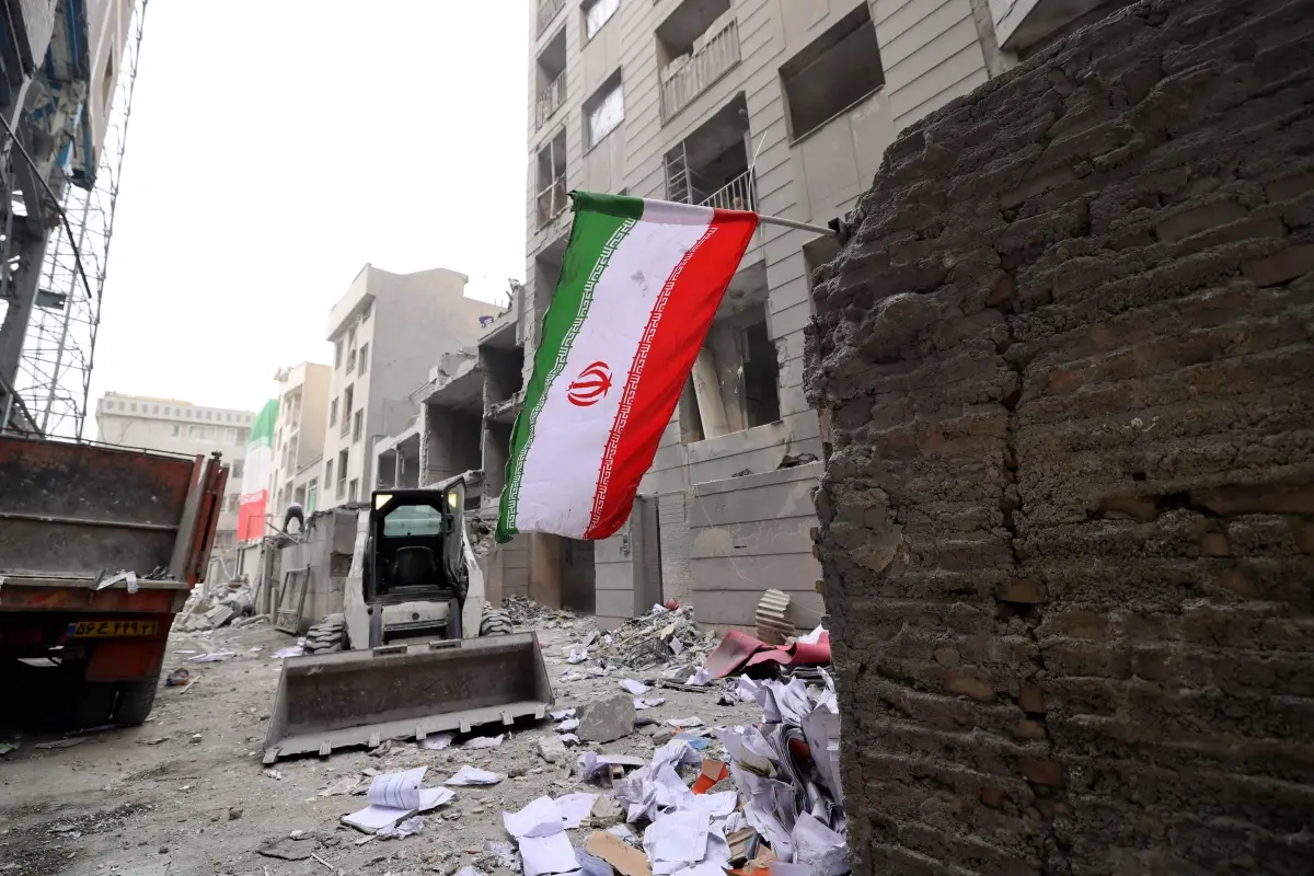 File Photo- An Iranian flag flutters as as digger arrives to help remove the debris from destroyed buildings following a military strike on the Iranian capital Tehran
