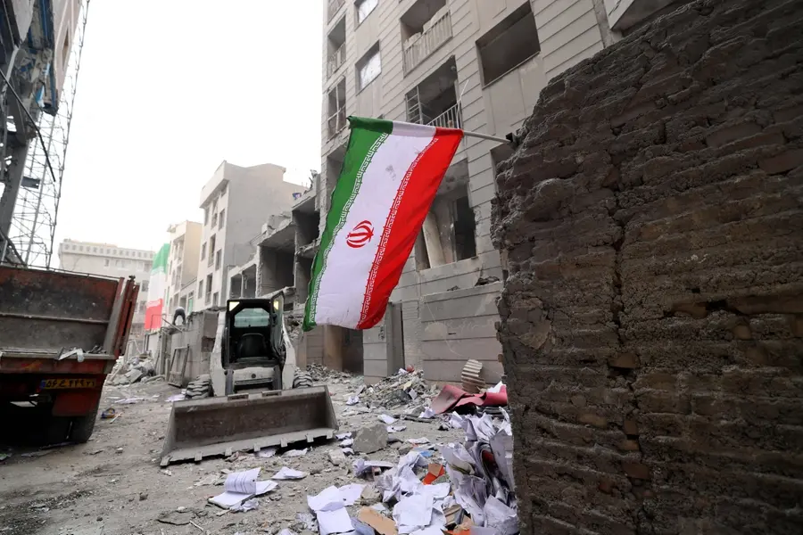 File Photo- An Iranian flag flutters as as digger arrives to help remove the debris from destroyed buildings following a military strike on the Iranian capital Tehran