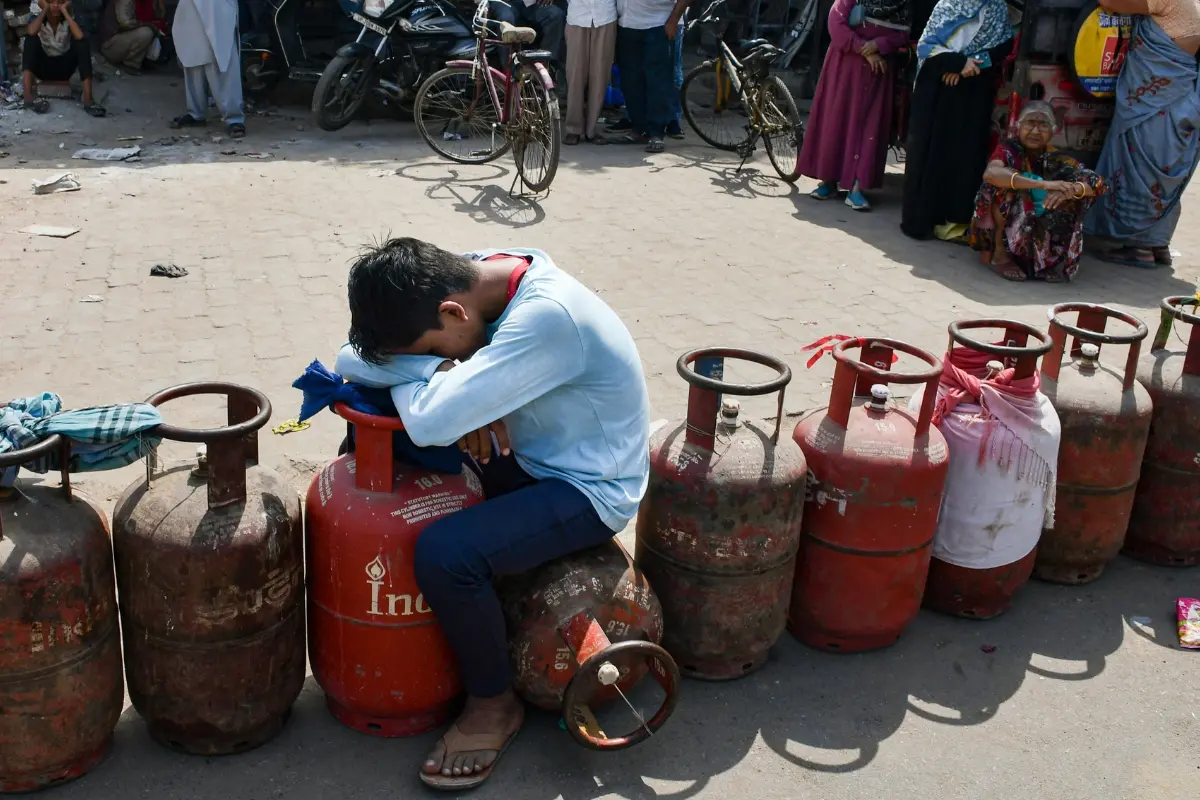 A child sits over an empty LPG cooking gas cylinder, as people arrive to avail refilled ones, amid a shortage linked to the ongoing West Asia conflict affecting the global energy supply chain, in Prayagraj | Photo: PTI