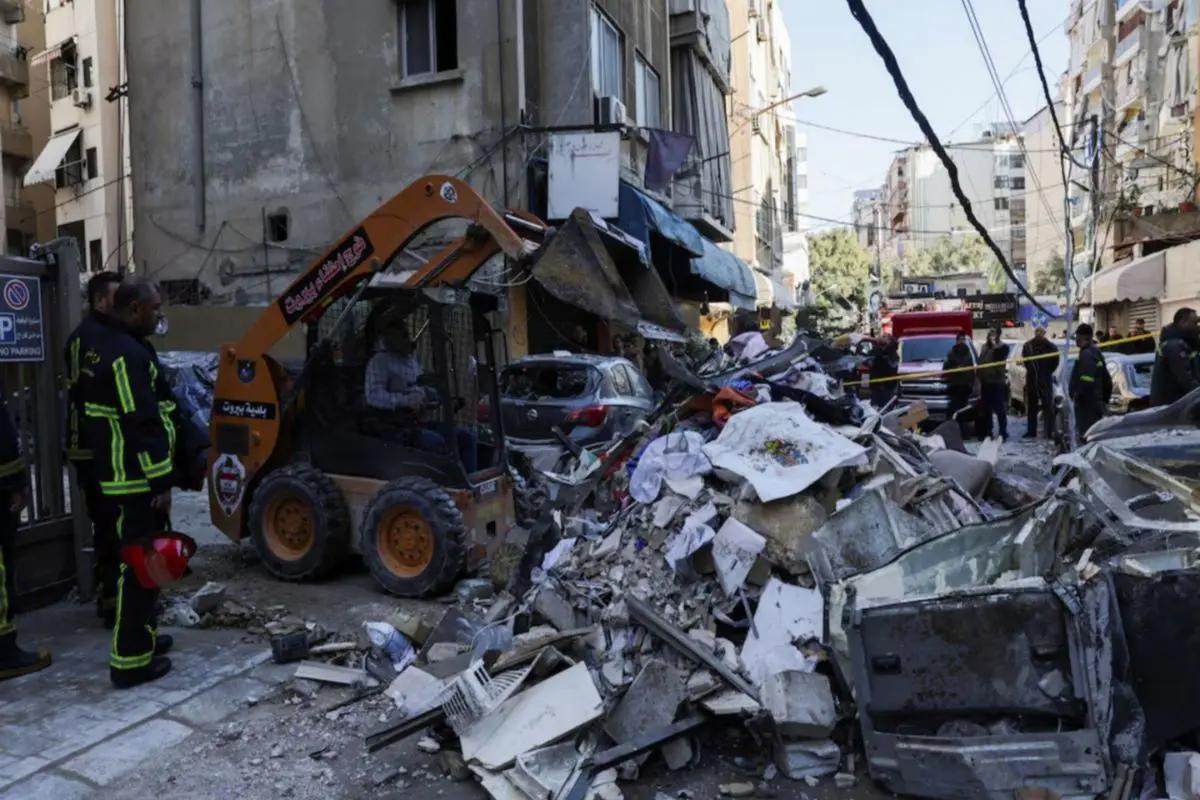 Emergency responders clear debris at a damaged site following a strike, as rescue teams and heavy machinery work amid destroyed vehicles and buildings.