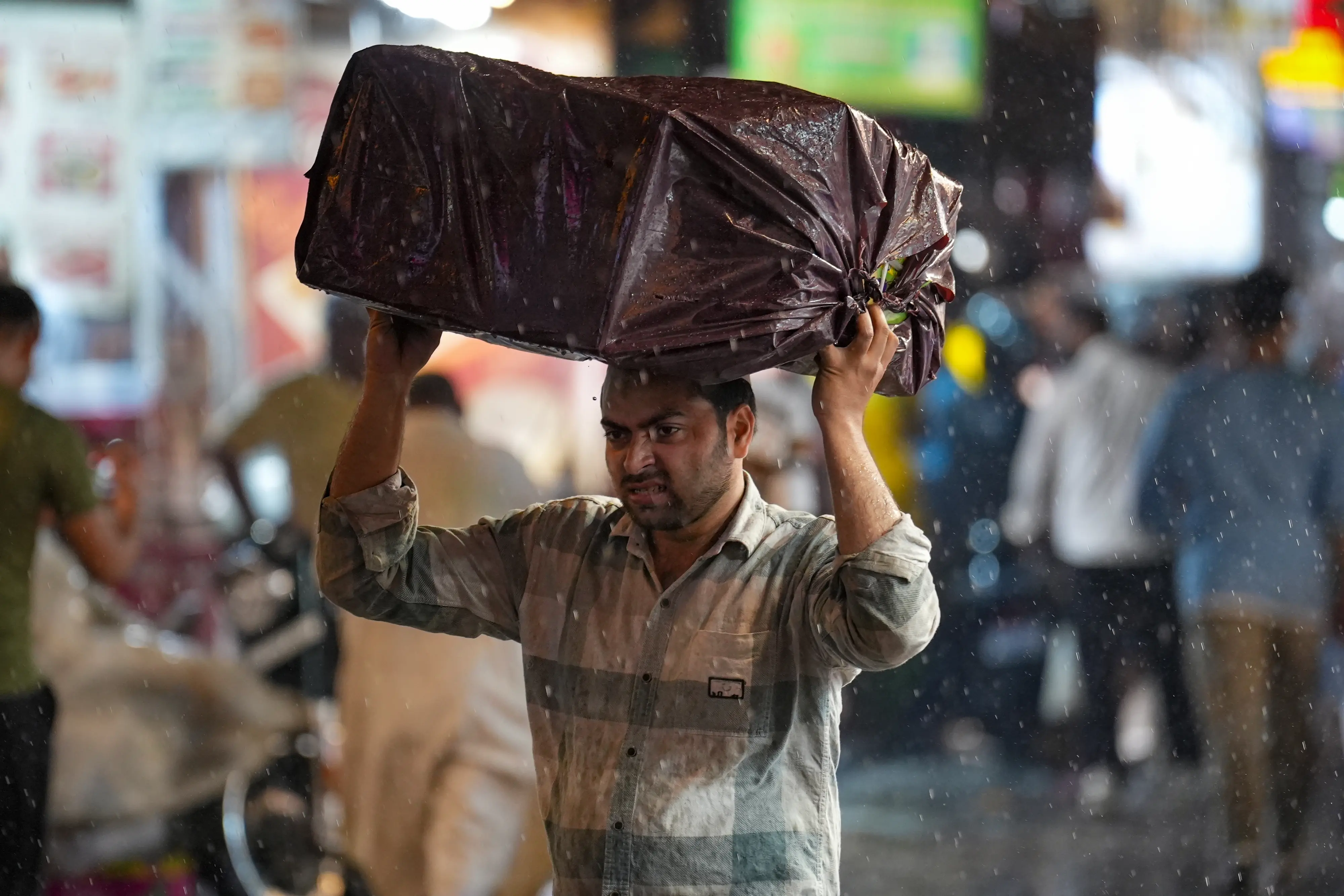 A man carries a covered package on his head amid rain at a market near Jama Masjid in New Delhi | PTI