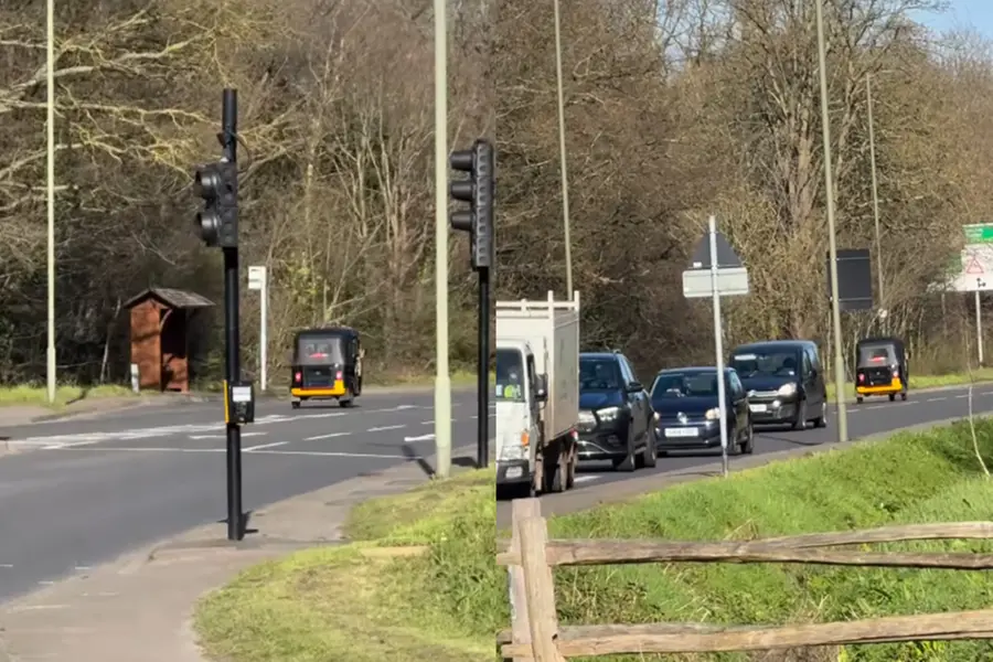 A distant shot of a auto-rickshaw cruising along a busy London road surrounded by European cars.