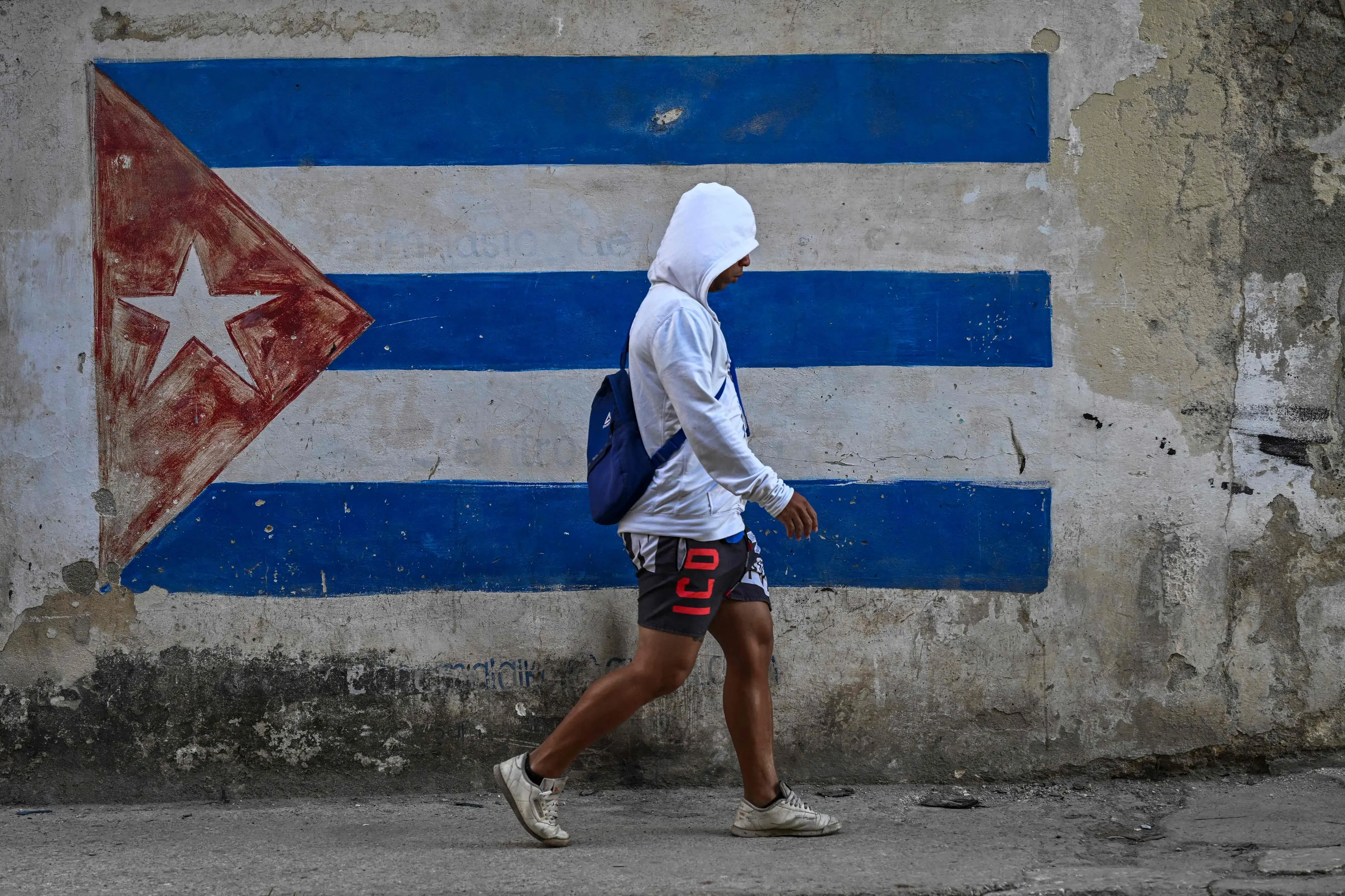 A man walks past a wall painted with a Cuban flag on a street in Havana during a nationwide blackout | AFP