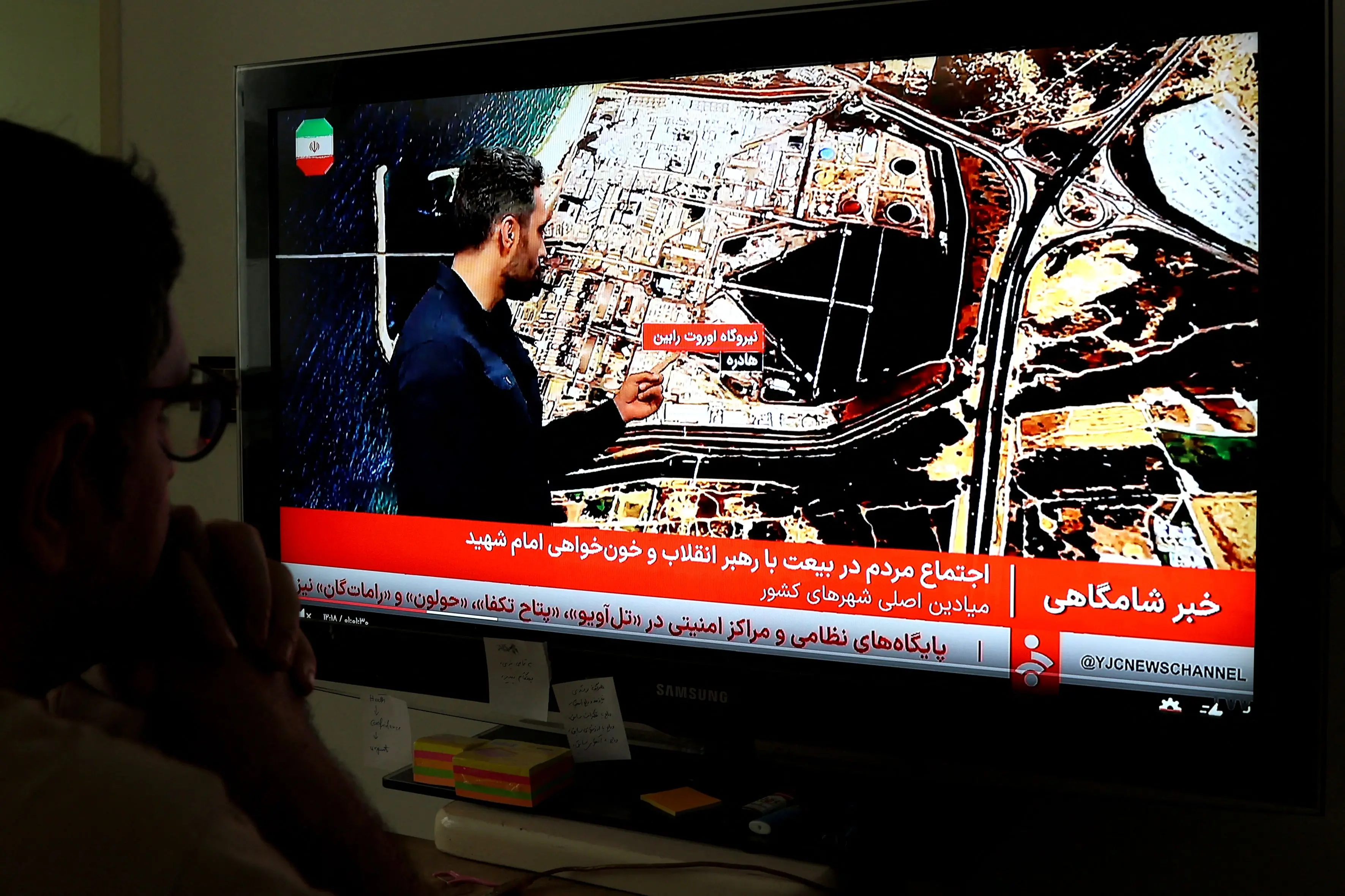 An Iranian man watches the news on Iranian State TV (IRIB) in Tehran on March 23, 2026. | AFP