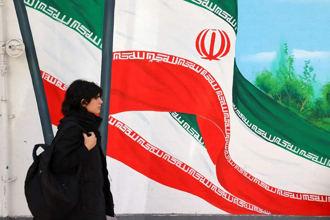 A woman walks past a mural painting of Iranian flags in a street in Tehran | Photo: AFP