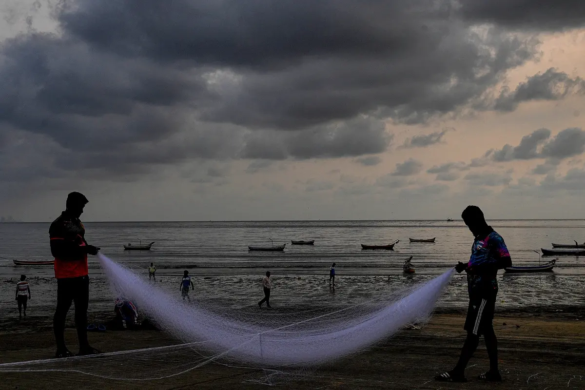 Fishermen spread out a net with dark clouds hovering in the backdrop, in Mumbai.| Photo:PTI