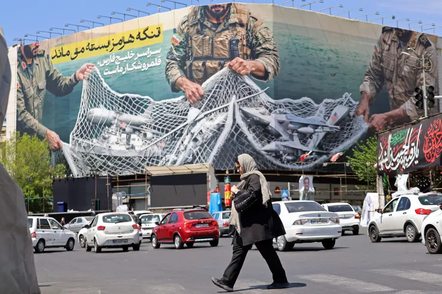 A woman walks past a giant billboard reading 'The Strait of Hormuz remains closed' at the Revolution Square in Tehran