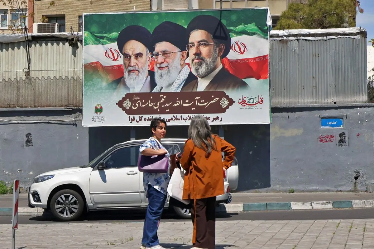 Women stand in front of a poster with portraits of Iran's late supreme leader Ayatollah Ali Khamenei (C), the late Ayatollah Ruhollah Khomeini (L) and the new supreme leader Mojtaba Khamenei, along a street in Tehran on April 12. Photograph: Atta Kenare/AFP