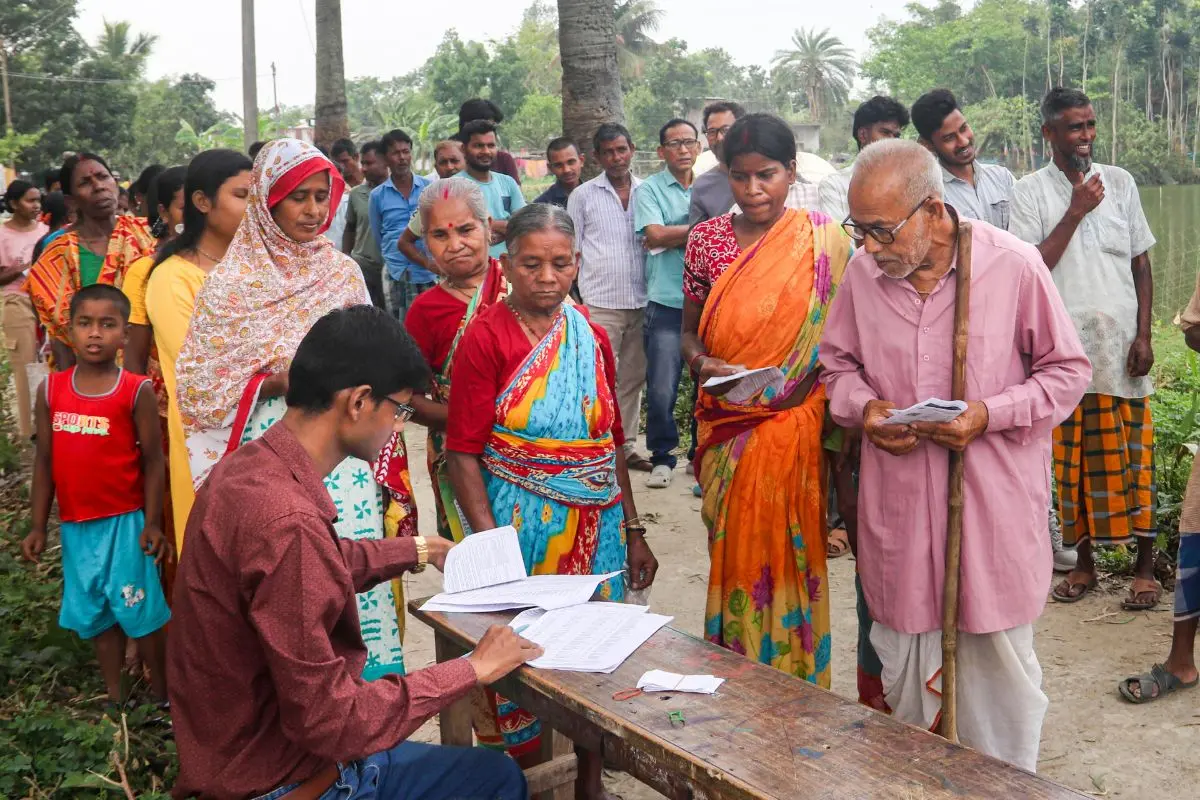 A poll official checks the names of the voters on a list as they wait in a queue to cast their votes in the first phase of West Bengal Assembly elections, at a polling station (Photo: PTI)
