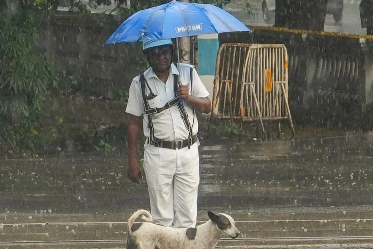 A traffic police personnel stands with a stray dog during rain, in Kolkata. (PTI Photo/Manvender Vashist Lav)
