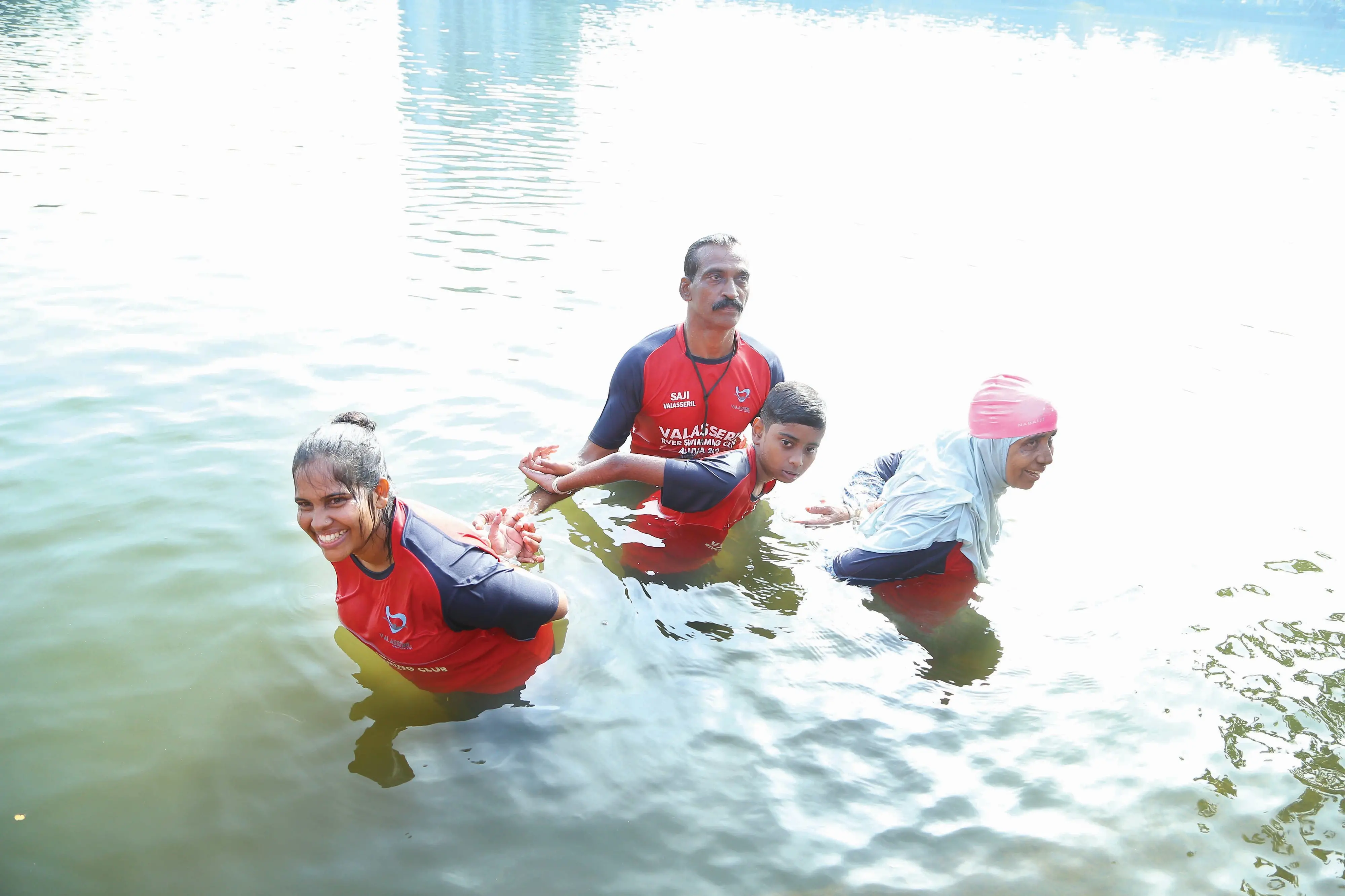 Participants demonstrate advanced water-survival skills by swimming across the Periyar River with their hands tied behind their backs alongside coach Saji Valasseril (C) in Aluva, Kerala.