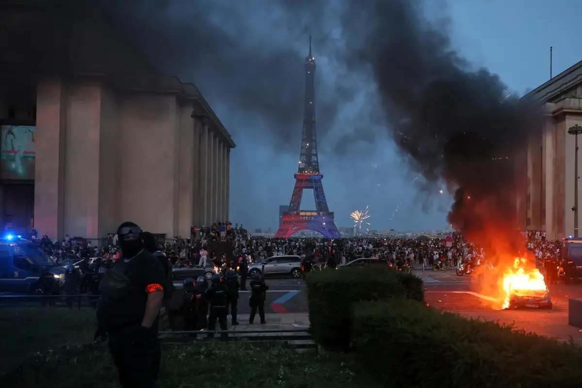 A car burns and fireworks explode as police watch PSG supporters celebrate in Paris