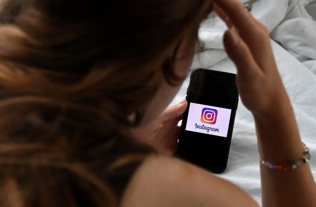In this photo illustration, a person looks at a smart phone with a Instagram logo displayed on the screen | Photo: AFP