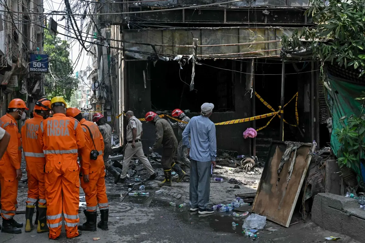 National Disaster Response Force (NDRF) personnel and firefighters stand at the site following a fire that broke out at a hotel in New Delhi
