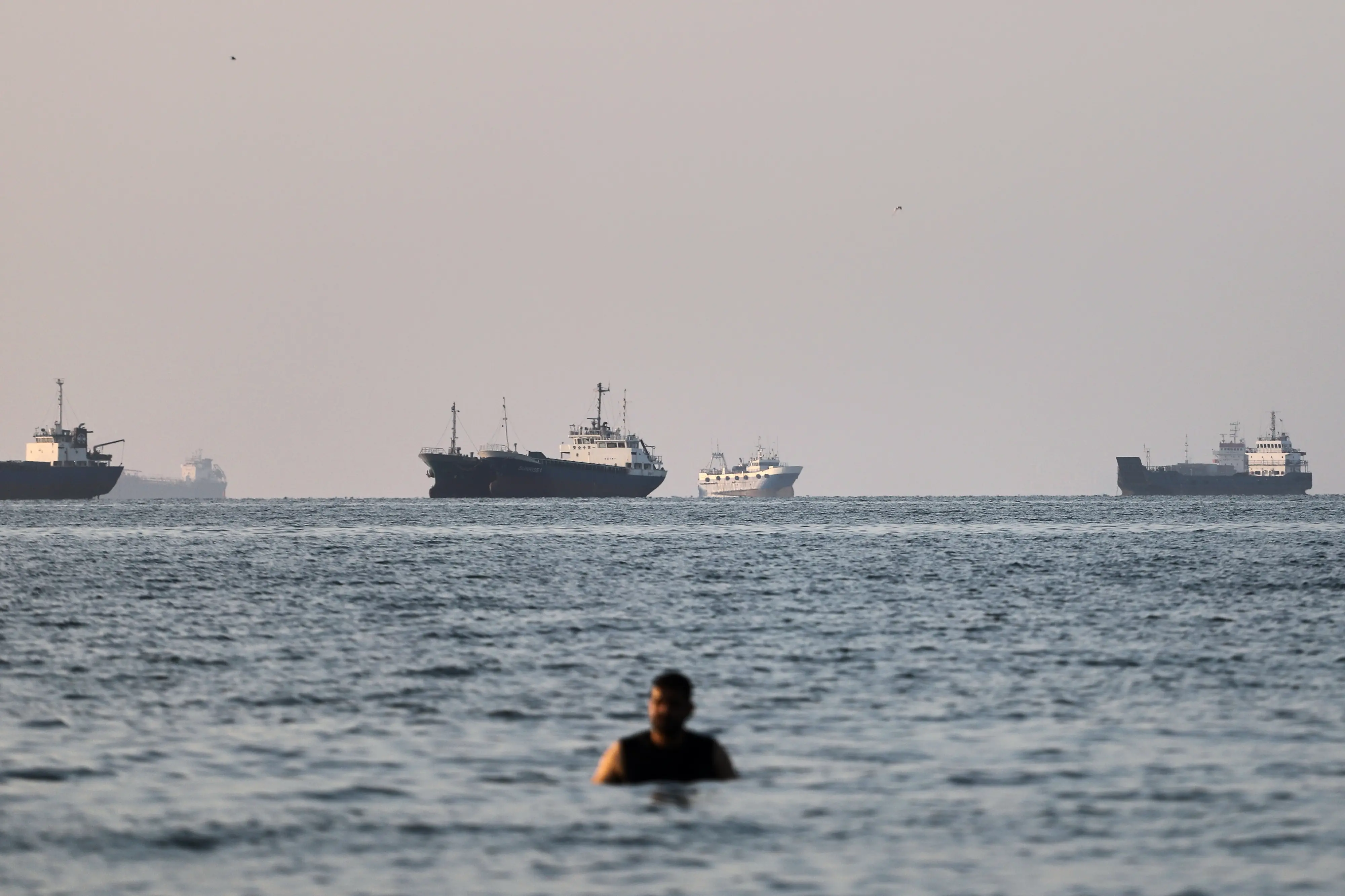 A person stands on shallow water as cargo and commercial vessels are anchored in the Strait of Hormuz off Bandar Abbas | AP