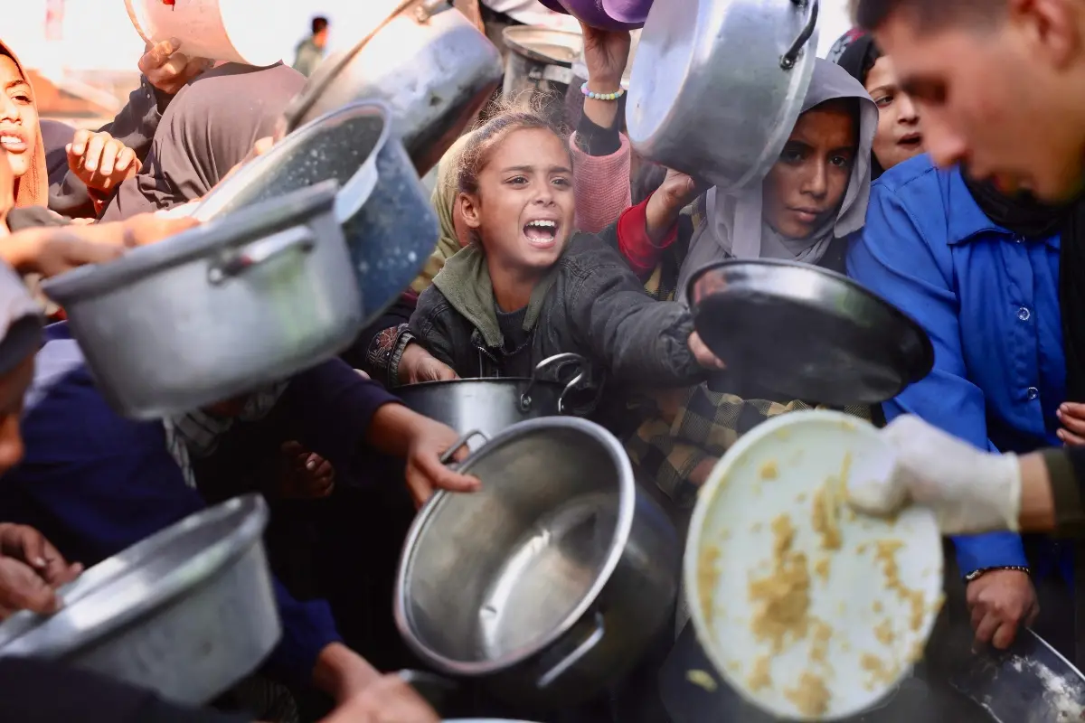 Displaced Palestinians gather to receive donated food portions at a charity kitchen in Khan Yunis in the southern Gaza Strip.| Photo: AFP