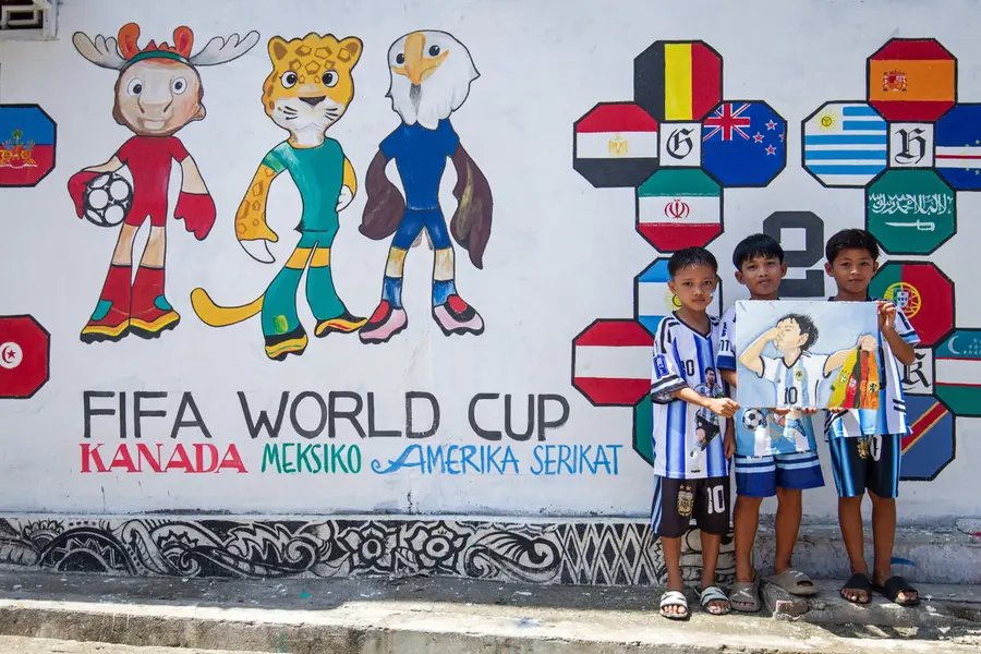 Children pose in front of a mural featuring the 2026 FIFA World Cup tournament on the eve of its start in Polewali Mandar in Indonesia's West Sulawesi