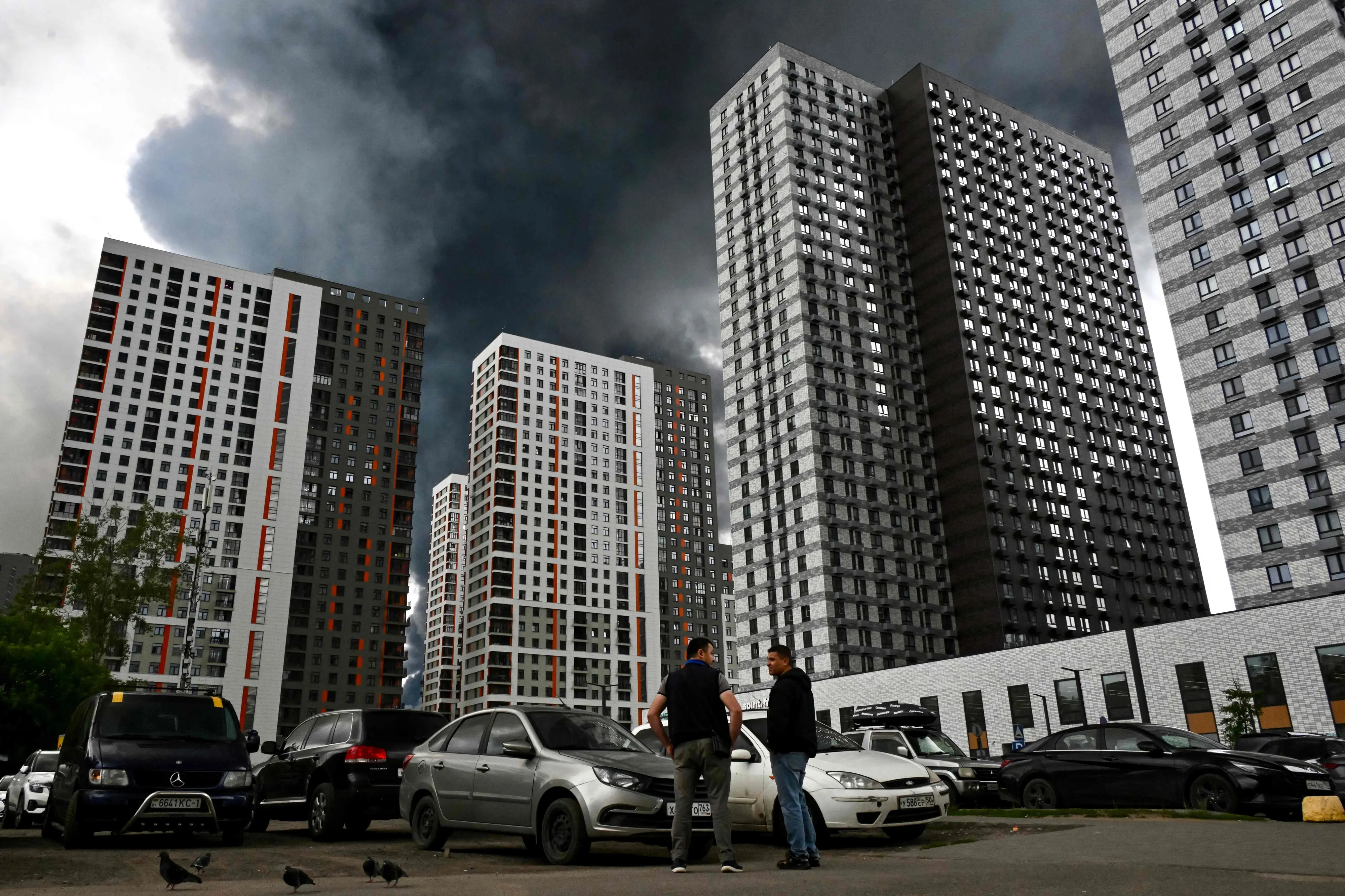 Men interact in a residential locality blanketed in black smoke in Moscow on June 18, 2026. Moscow was fending off a "large-scale" drone attack from Ukraine, with several drones reaching an oil refinery, the city's mayor Sergey Sobyanin said early on June 18, 2026. (Photo by AFP)