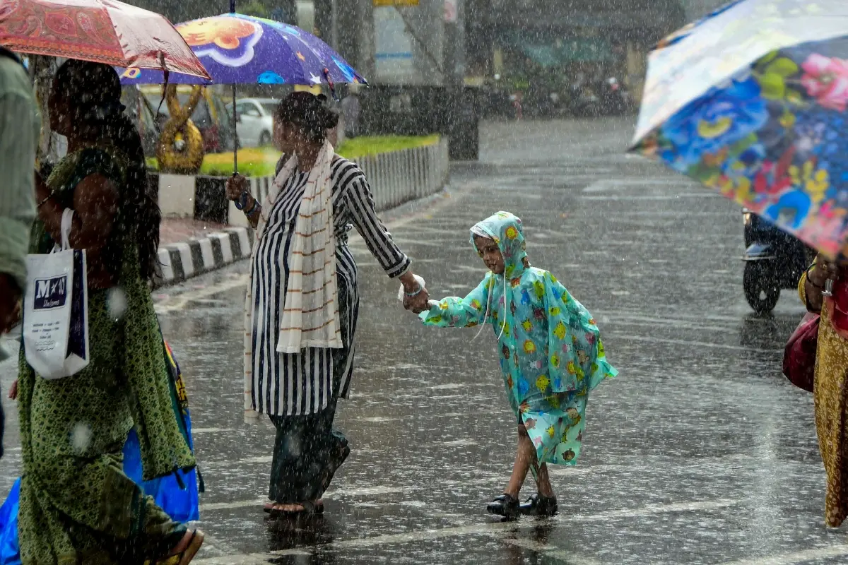 People cross a road under umbrellas during heavy rainfall, in Mumbai.| Photo: PTI