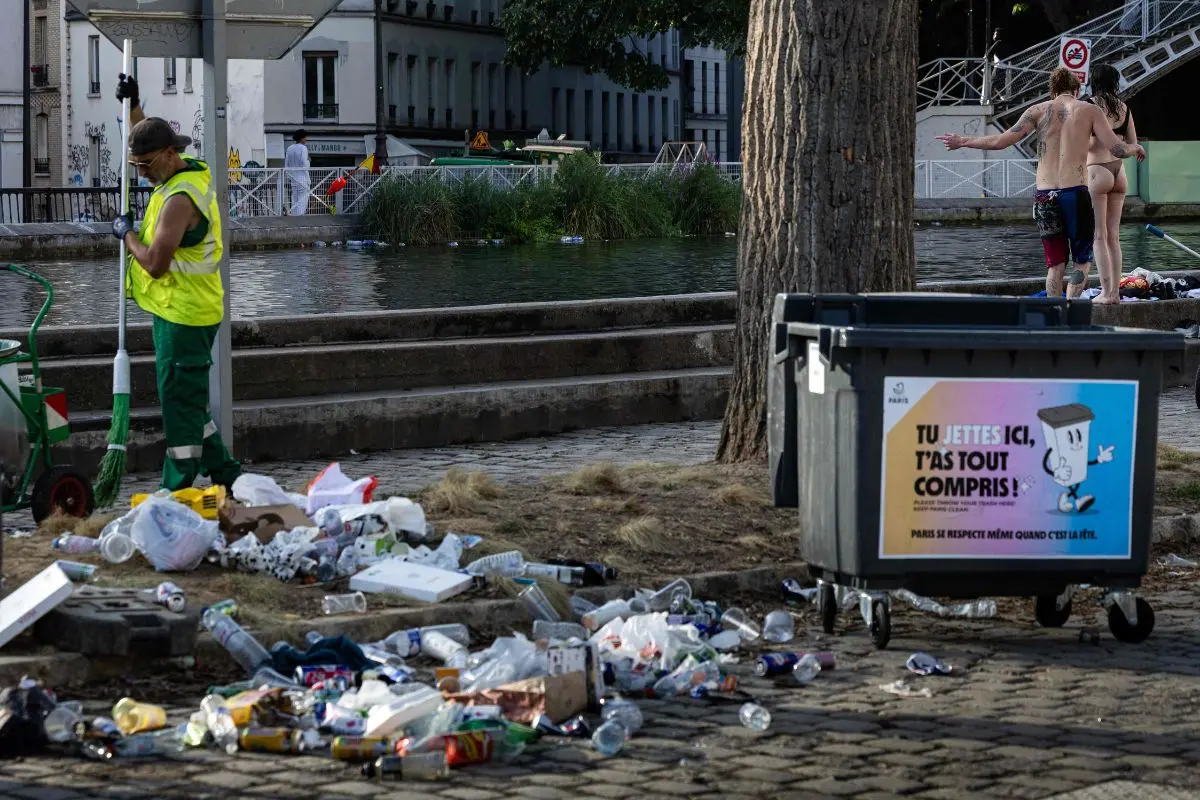 Municipal workers clean up food and drink waste on the banks of the Canal Saint-Martin in the background on the morning following the national annual street music festival 'Fete de la Musique' in Paris on June 22, 2026. (Photo by JOEL SAGET / AFP)
