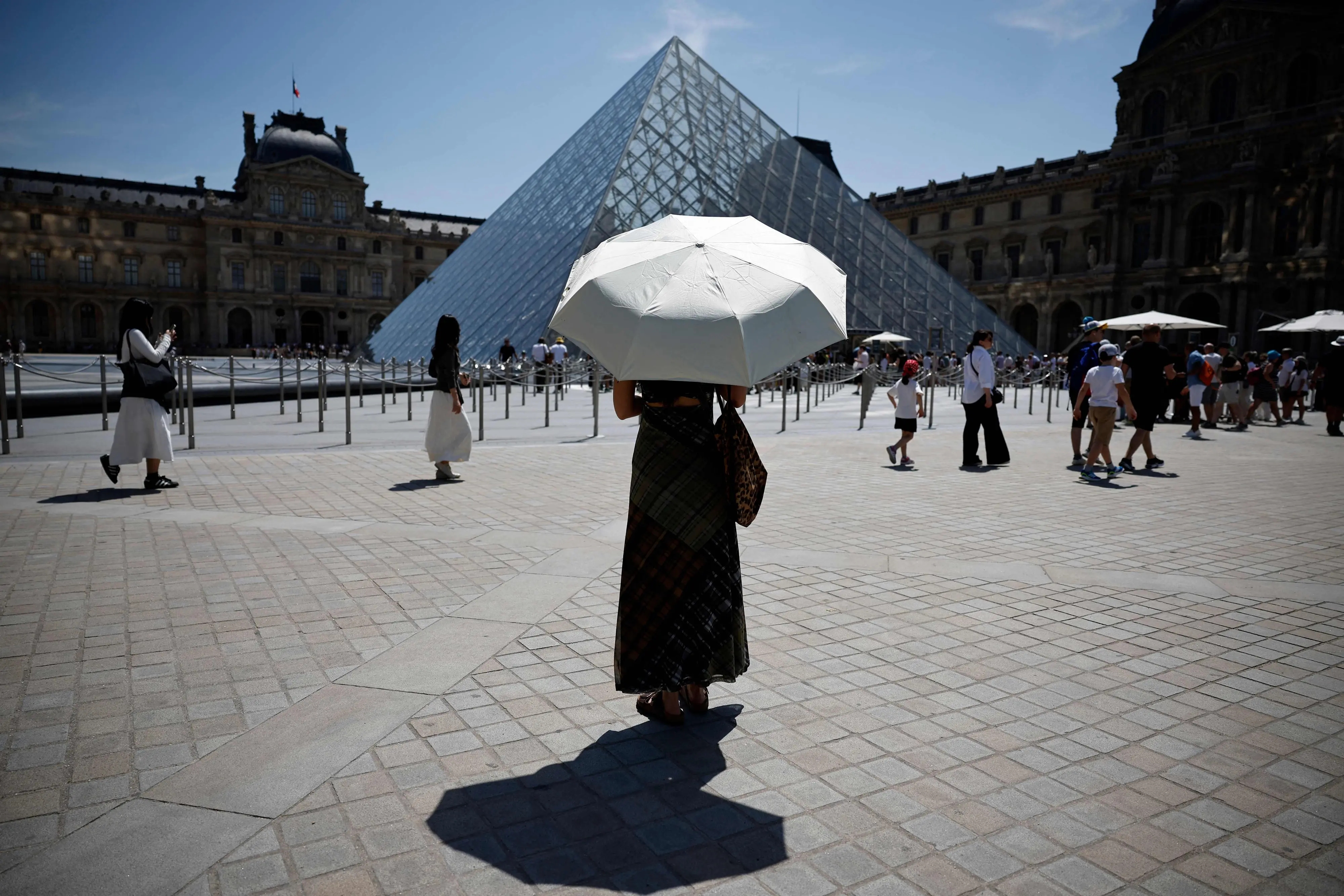 A person protects from the sun under an umbrella in front of the Louvre museum in Paris as a record-breaking early heatwave scorches a swathe of western Europe.| Photo: AFP